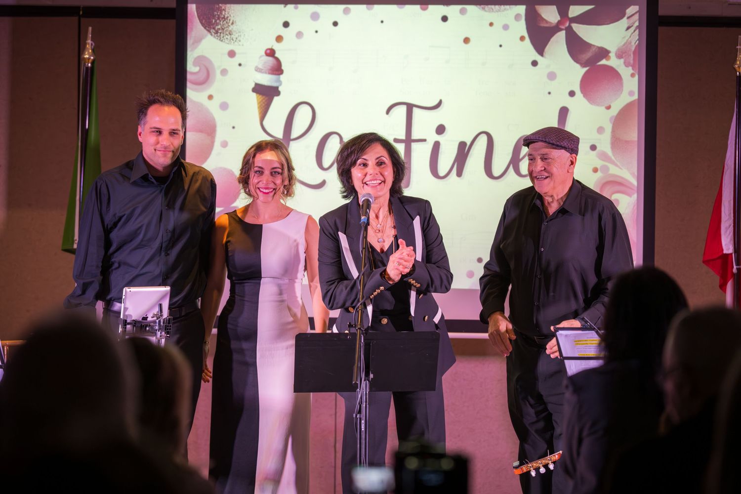 Four performers take a bow on stage in front of a La Fine projection screen at show finale.