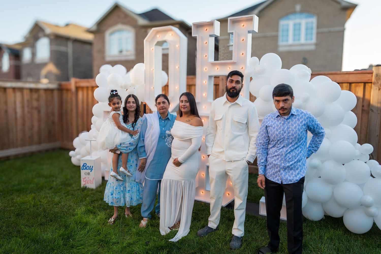 Family group photo at outdoor gender reveal party with OH BABY marquee sign at dusk.