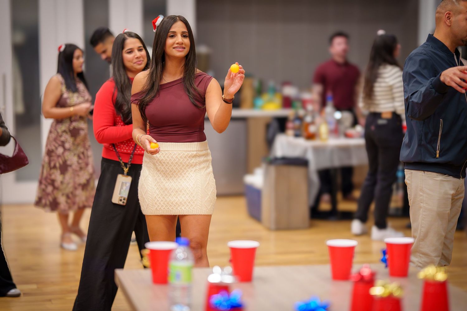 Party guests gather around red cups on a table during an indoor social event.