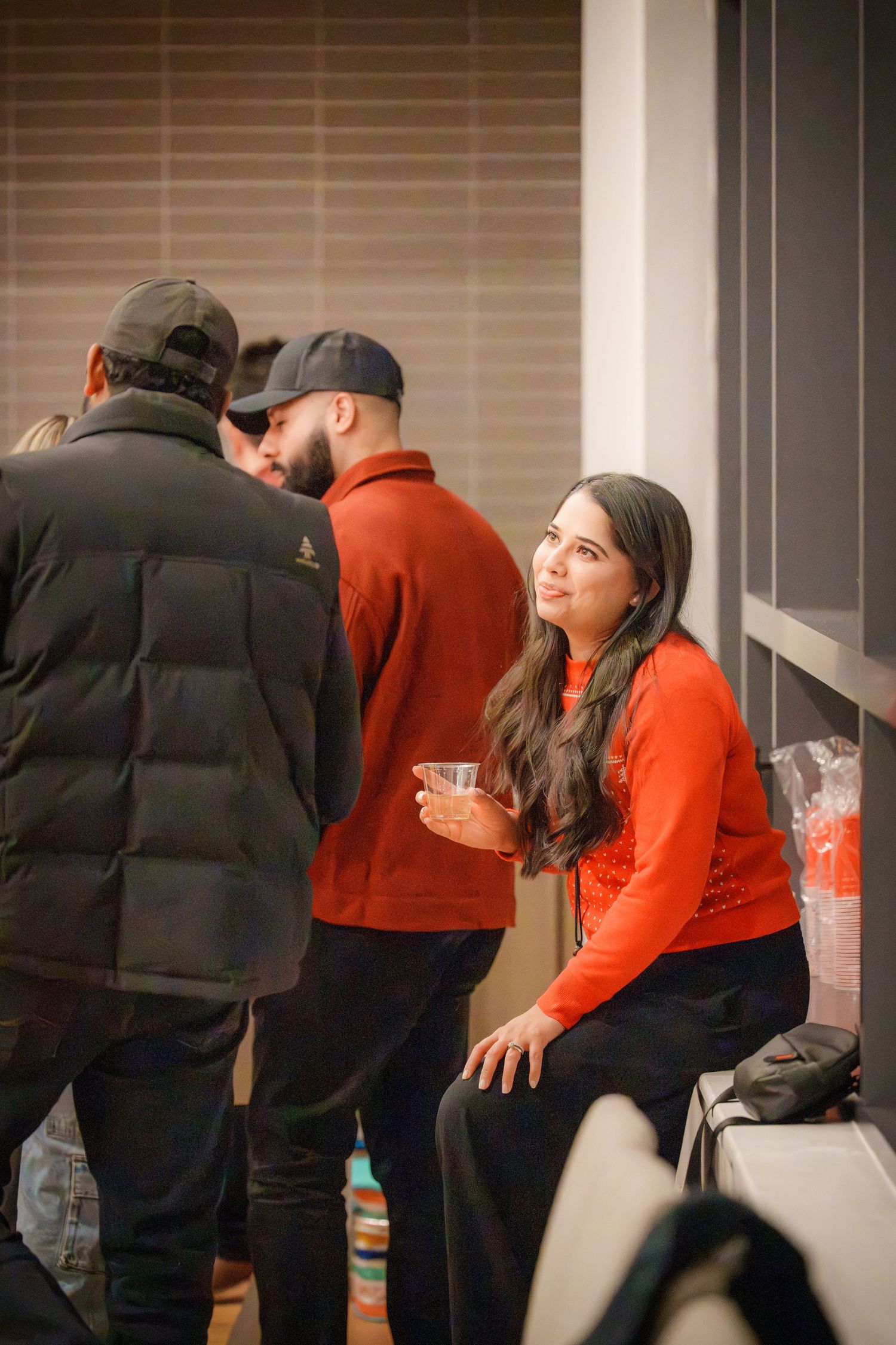 Three people chatting at an indoor gathering, with two wearing black and red casual attire.