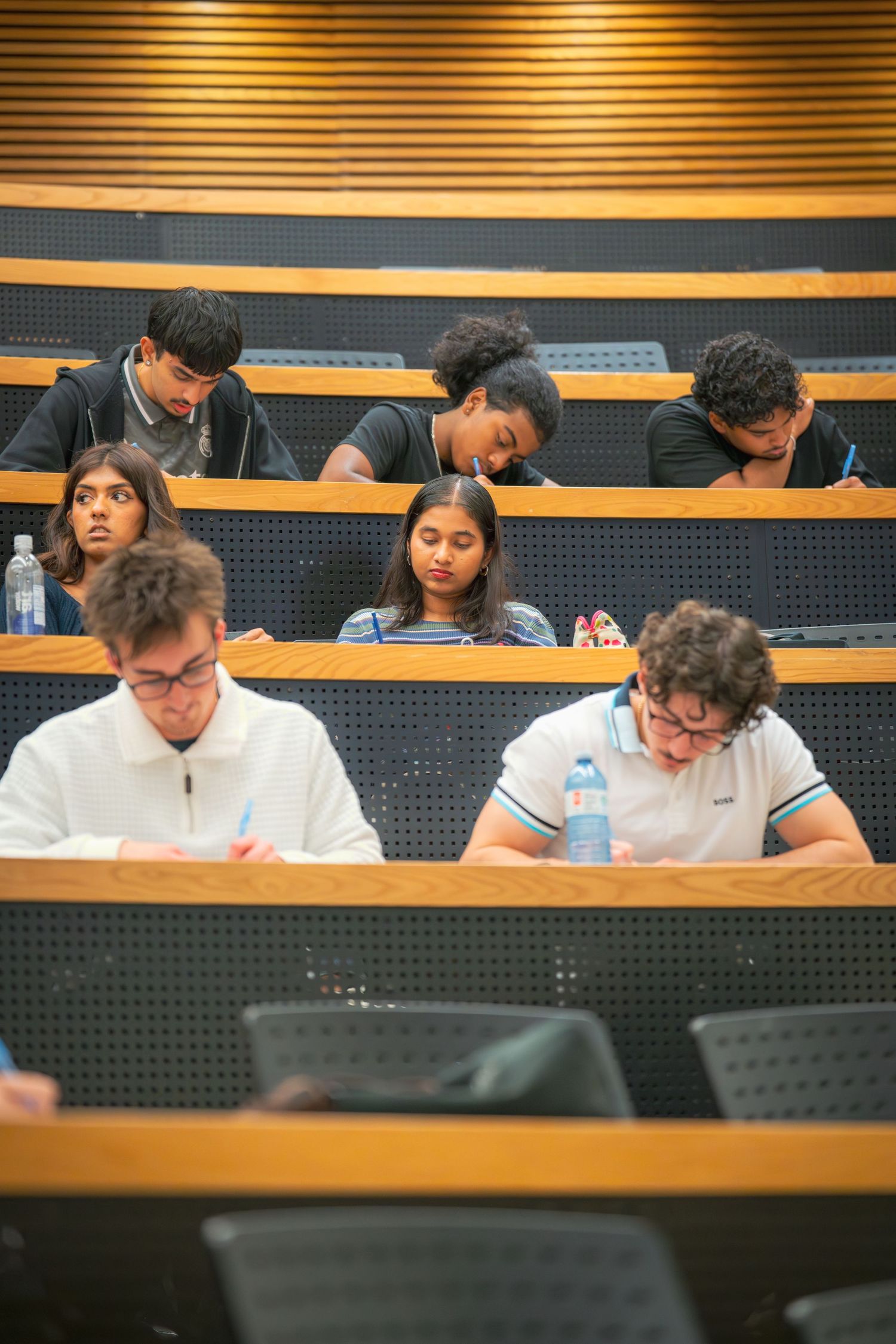 Students seated in curved rows take notes during a classroom session.