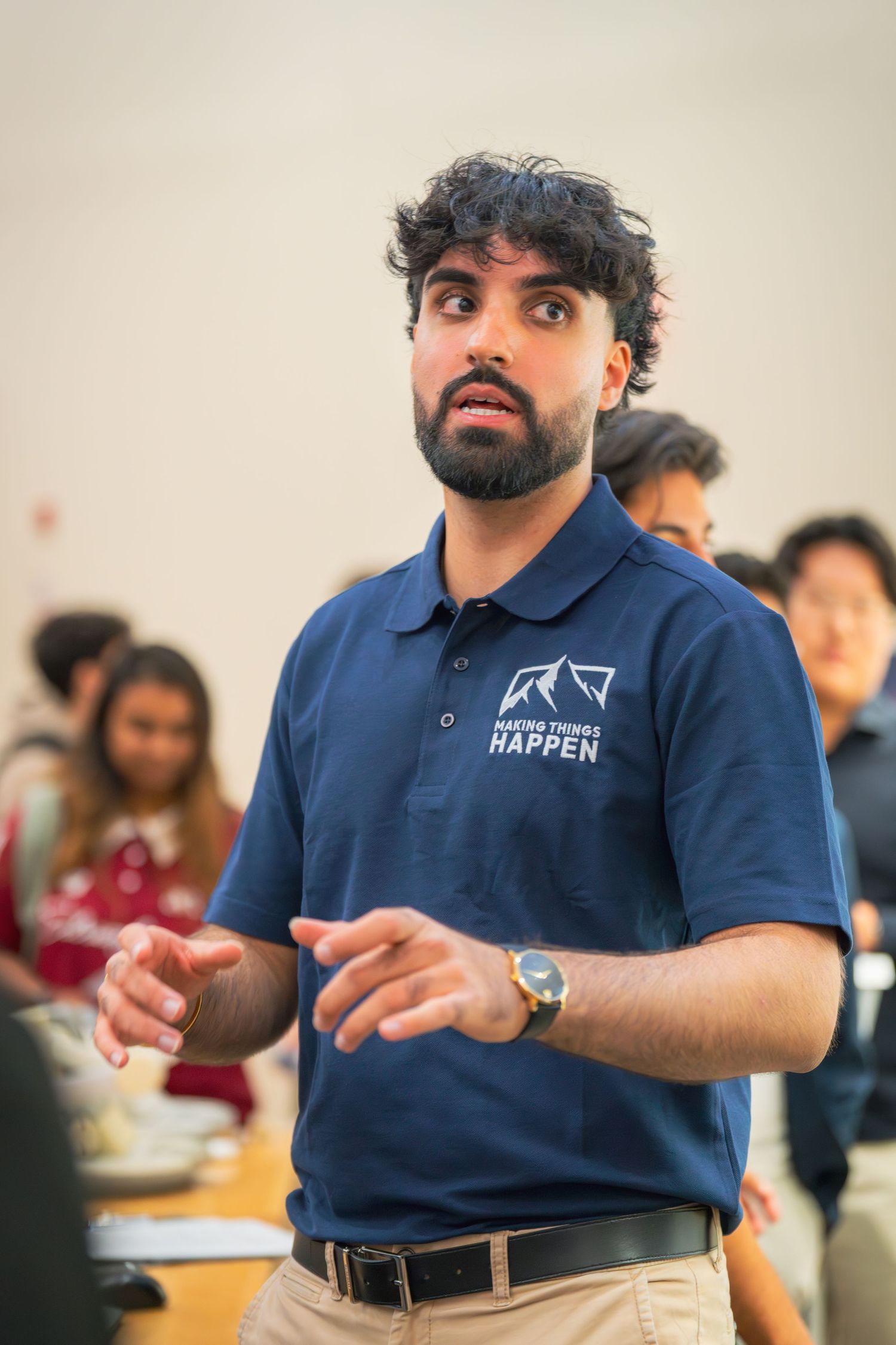 A presenter in a navy polo shirt gestures while speaking during an educational session.