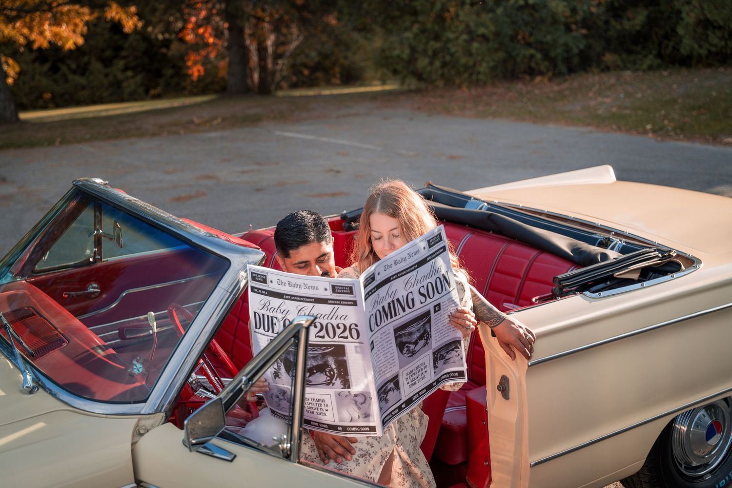 A vintage convertible car with newspapers on the passenger seat drives down a tree-lined road at sunset.