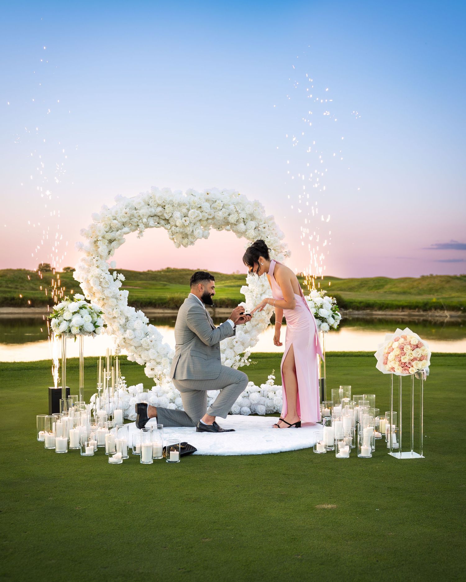 Intimate proposal moment captured on a golf course surrounded by white flowers and glowing candles.