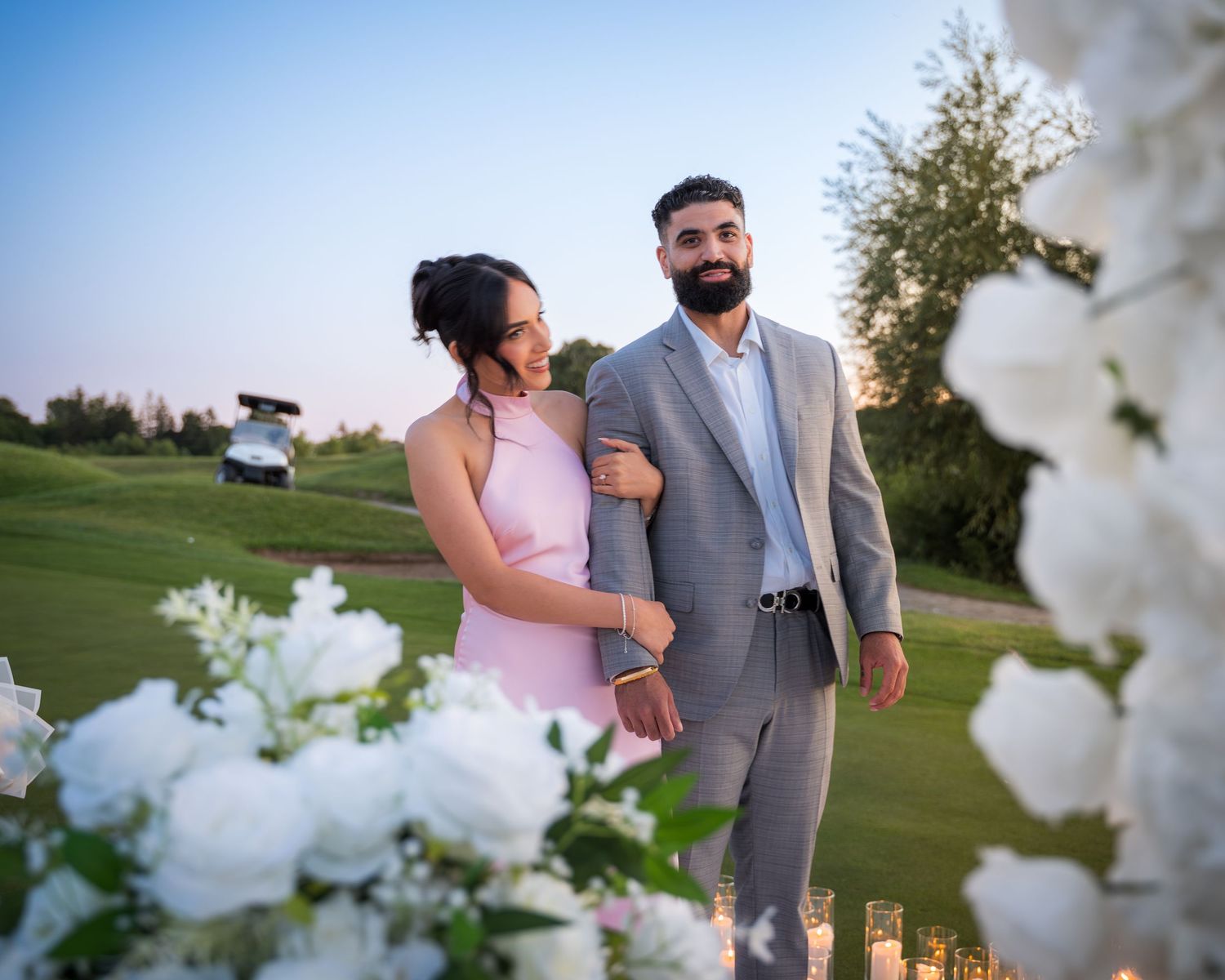 Romantic couple embraces during sunset at an outdoor venue with floral decorations.