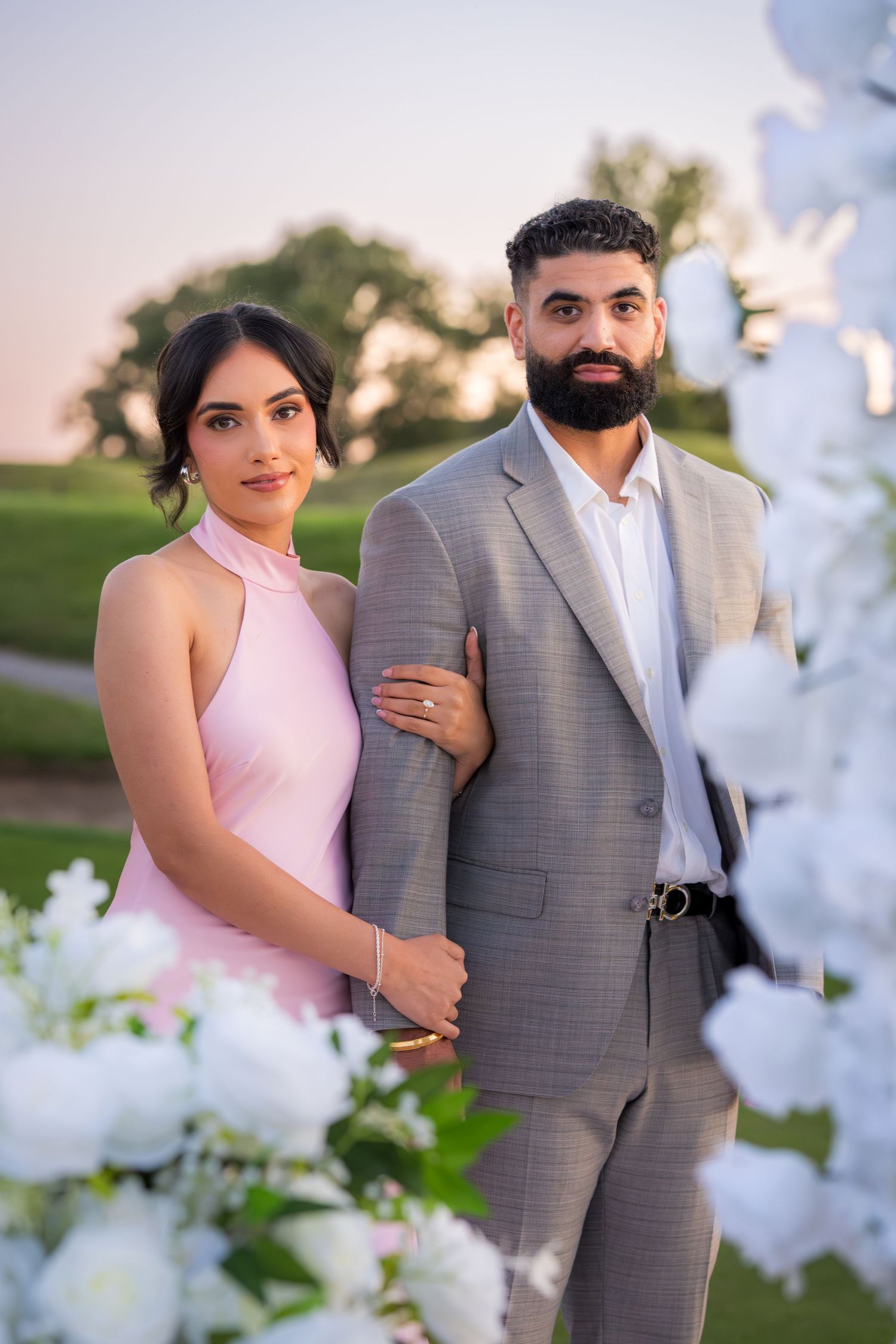 A romantic couple poses together outdoors with white smoke effects in a pink and grey color scheme.