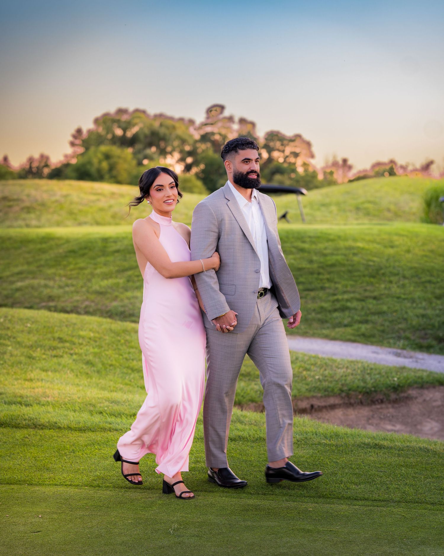 Couple strolling hand in hand across a scenic golf course at dusk.