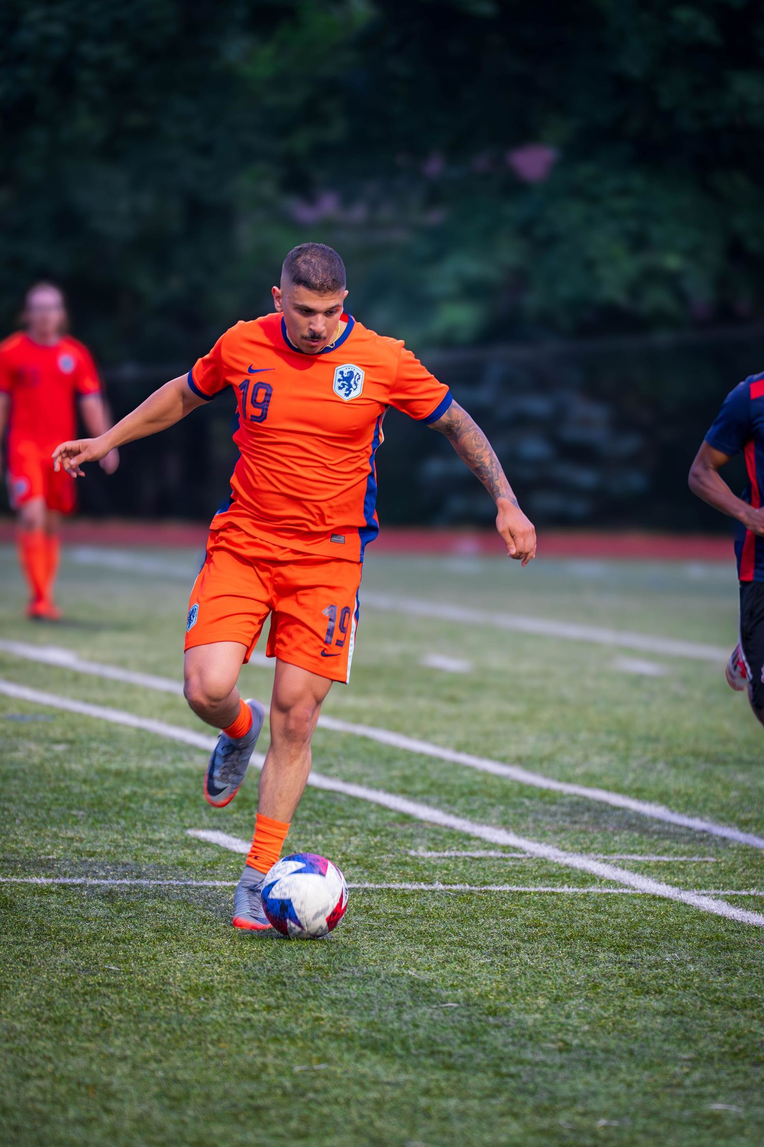 Soccer player in orange jersey prepares to strike ball during game action.