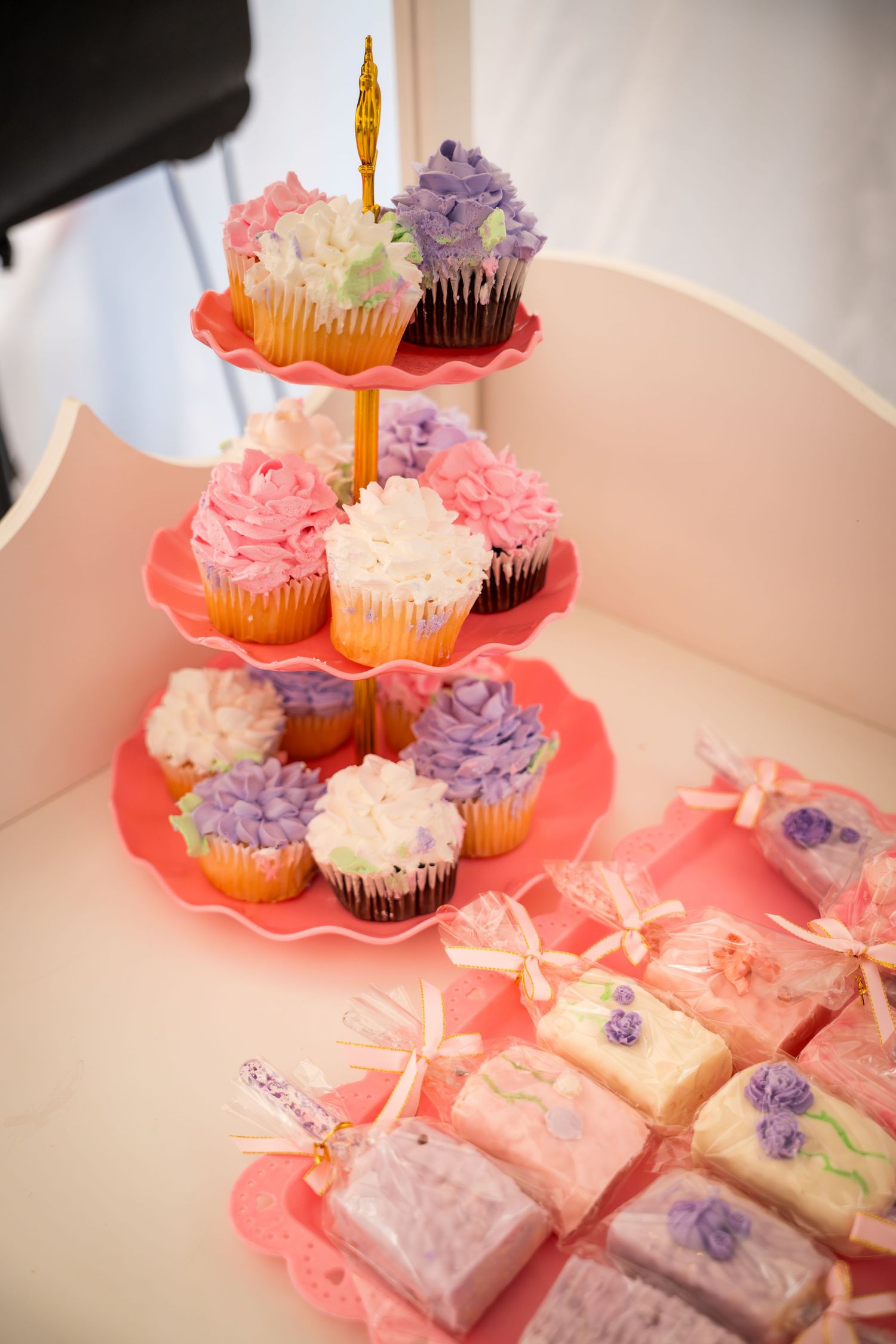 Pink and purple cupcakes displayed on a tiered stand with decorated gift boxes.