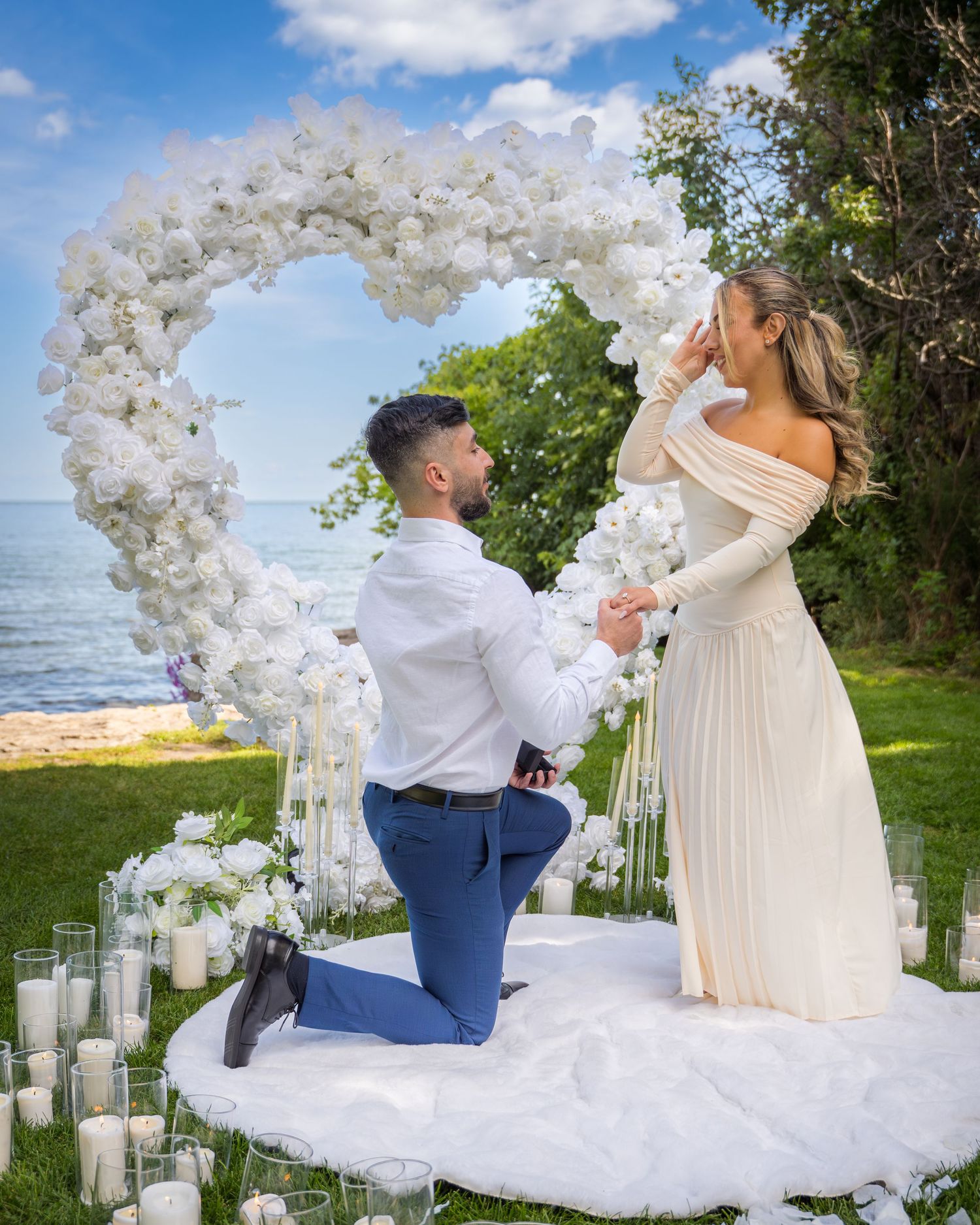 Elegant outdoor proposal scene with white balloon decorations and scattered candles in glass holders.