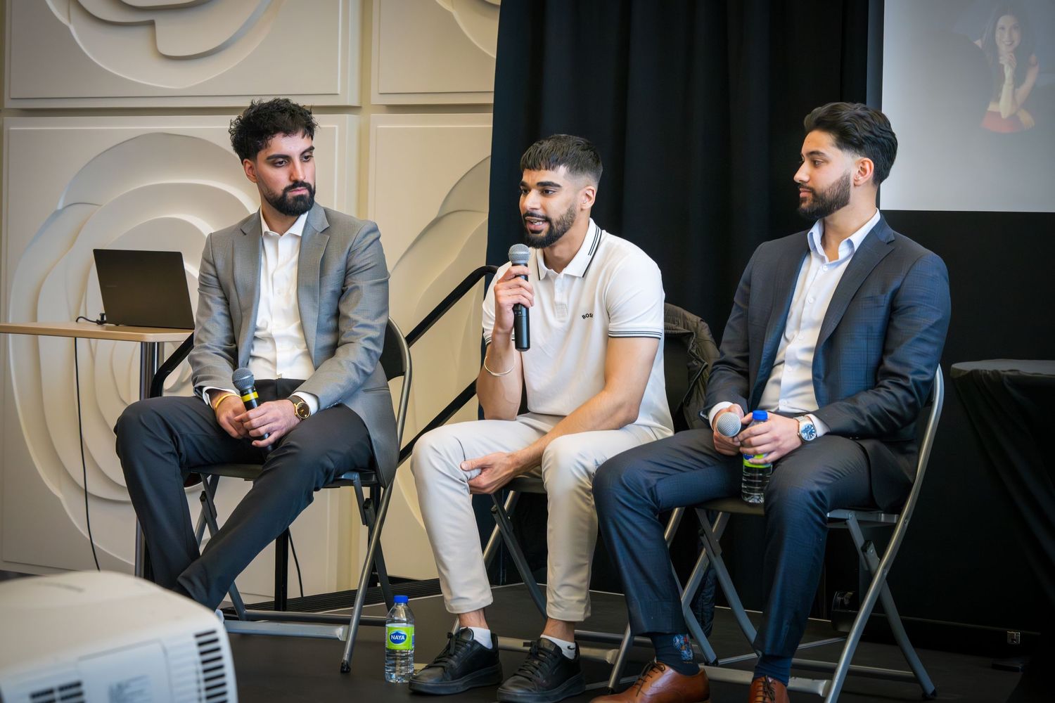 Three panelists in business attire seated on stage during professional discussion event.