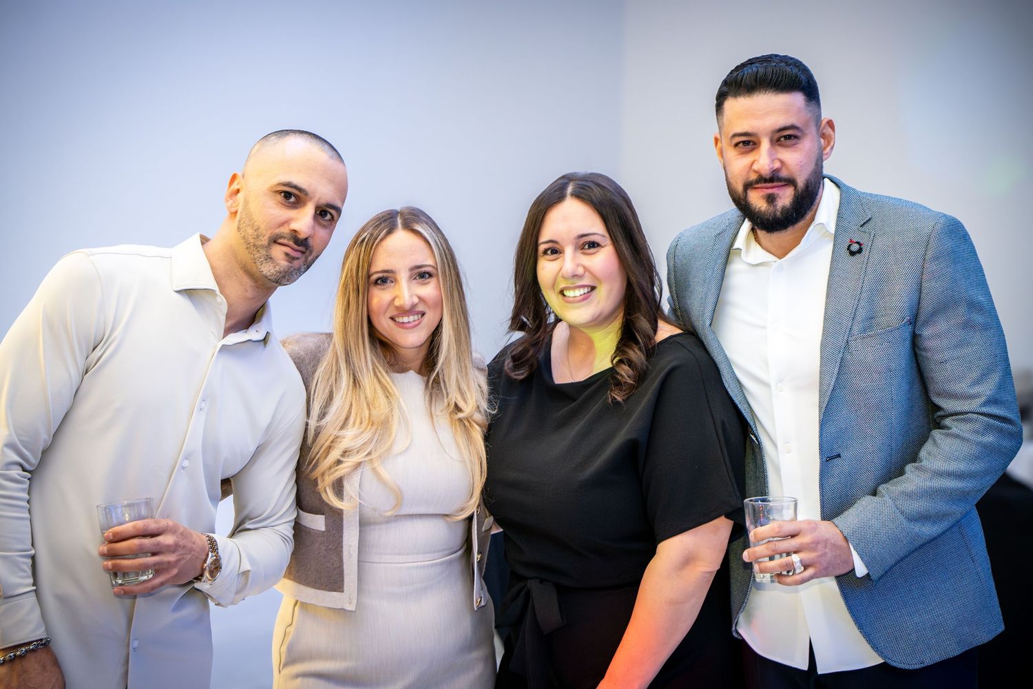 Two couples posing together at a formal event against a light gray background.