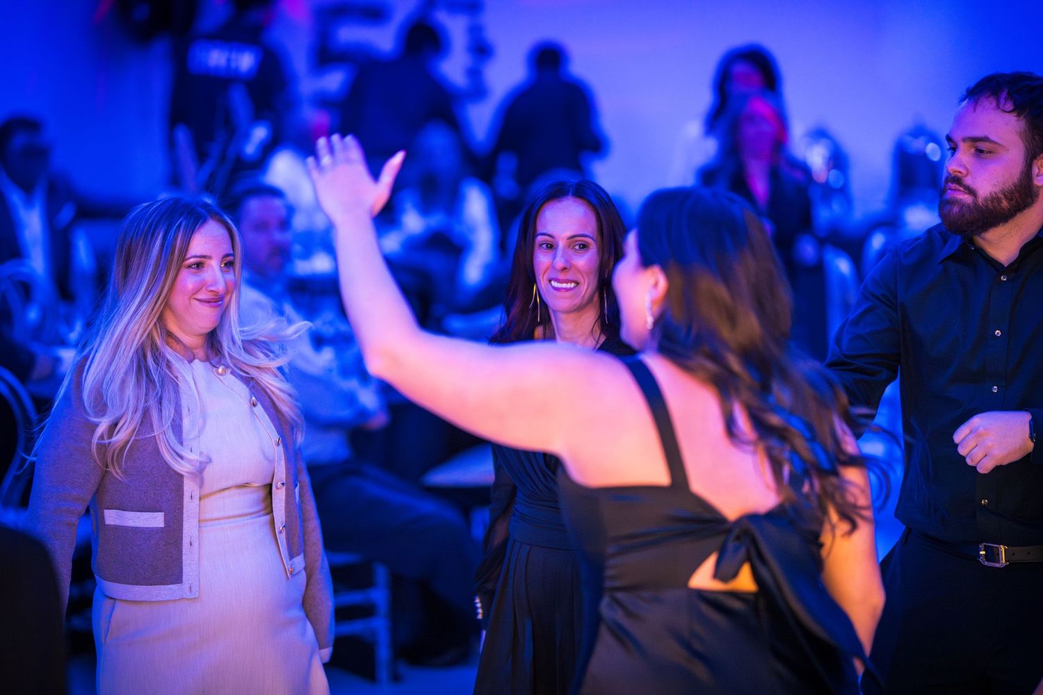 People dancing and celebrating in a dimly lit venue with blue atmospheric lighting.