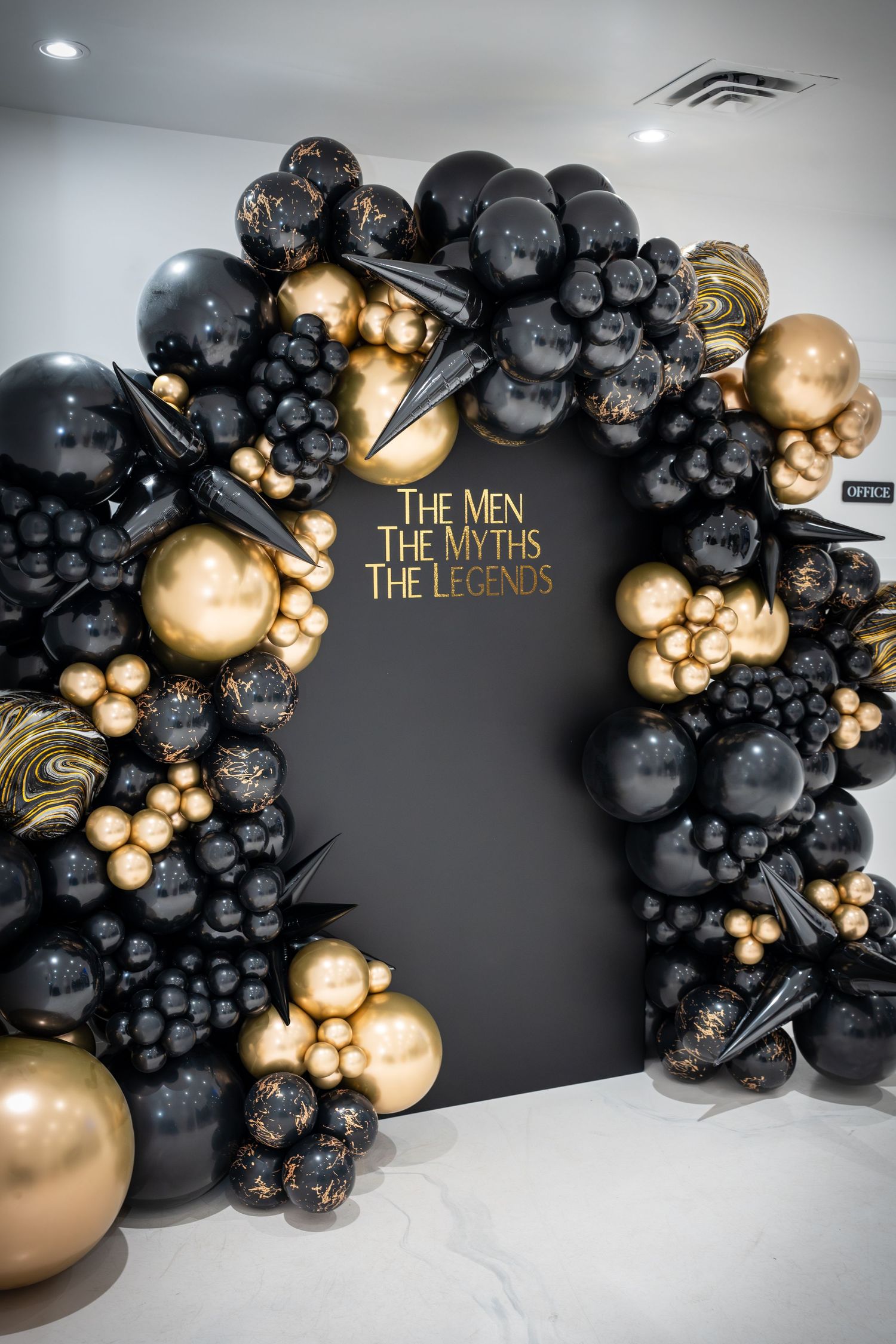 Elegant black and gold balloon arch installation against dark wall.