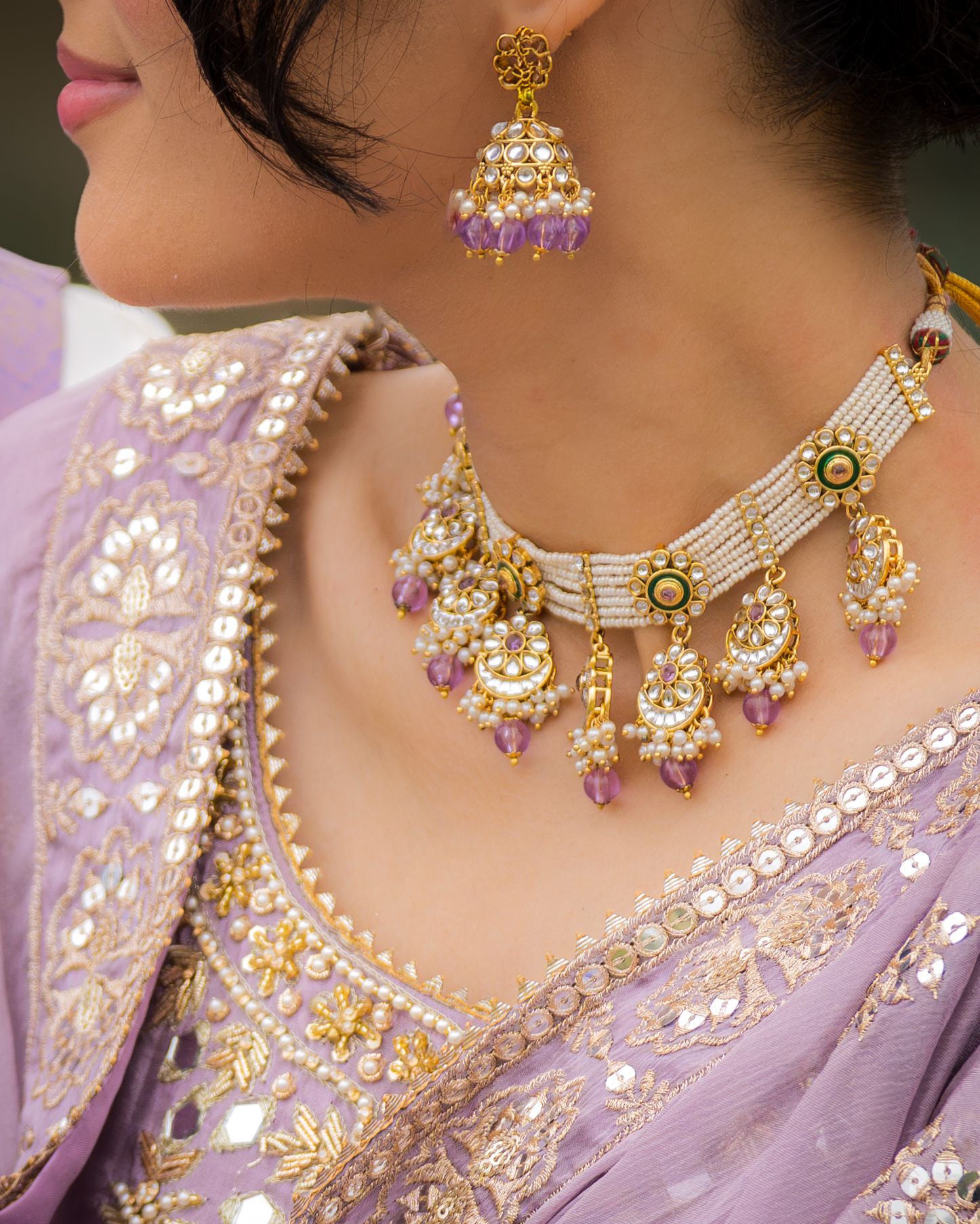 Close-up details of ornate gold and pearl jewelry with purple accents on lavender fabric.