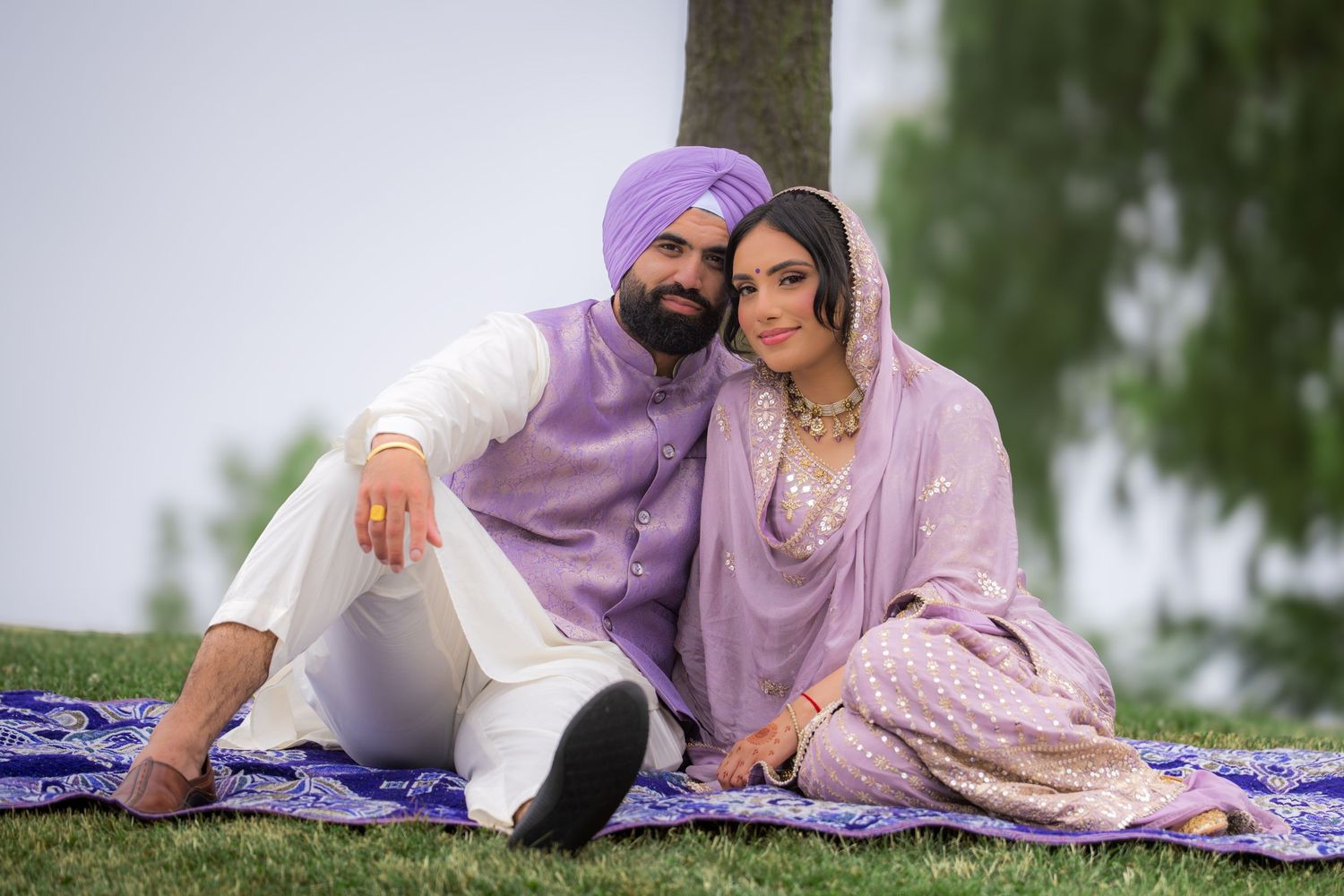 Three people in traditional Indian attire pose together on a blue patterned blanket in an outdoor setting.