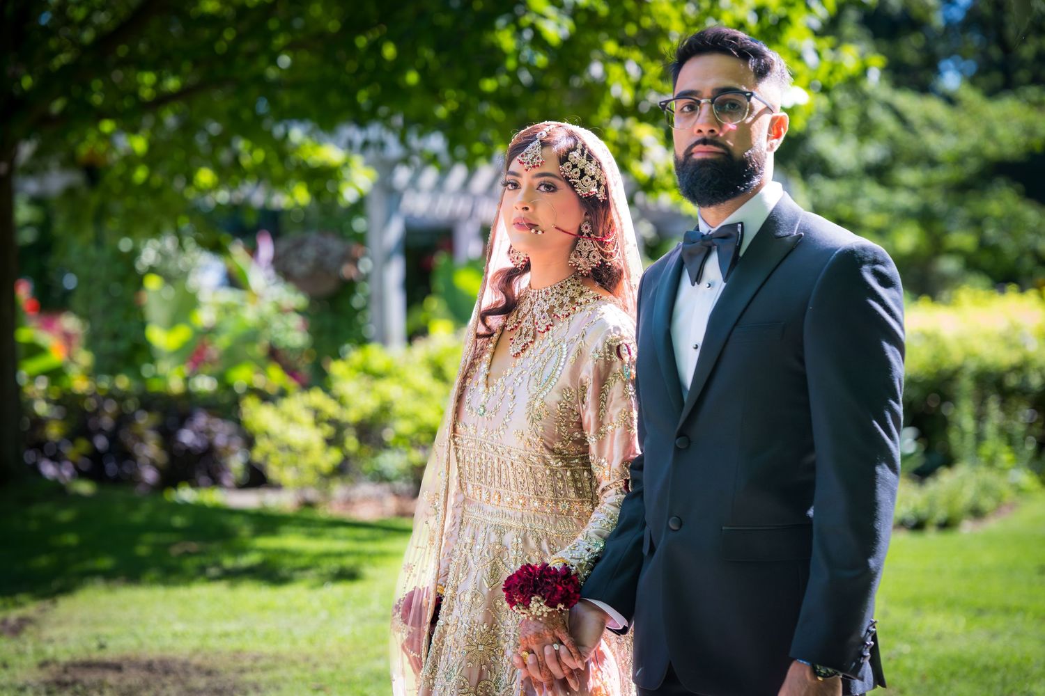 Elegant outdoor wedding ceremony with couple in traditional South Asian dress against natural greenery.