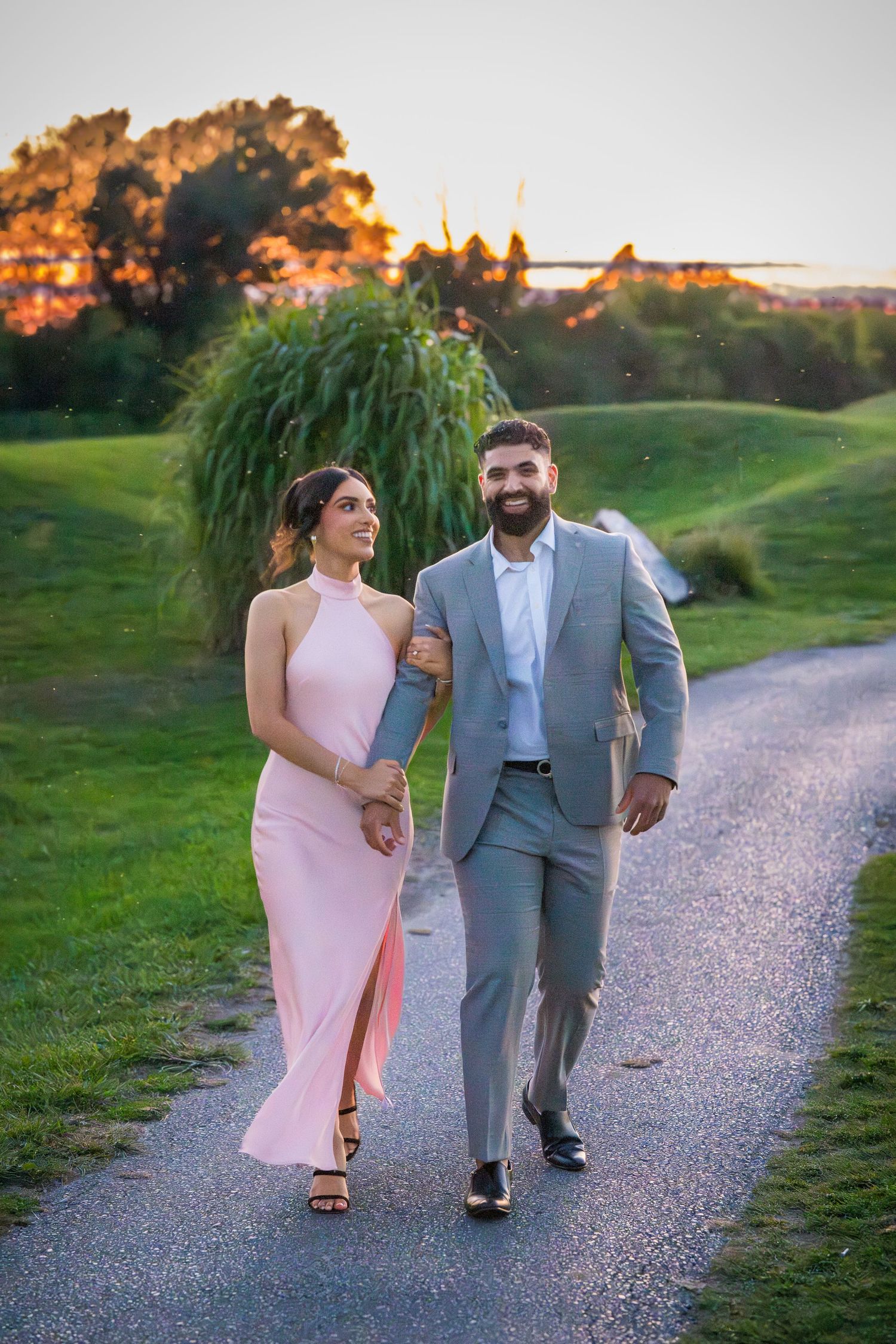 Romantic couple walking hand in hand on gravel path during sunset.