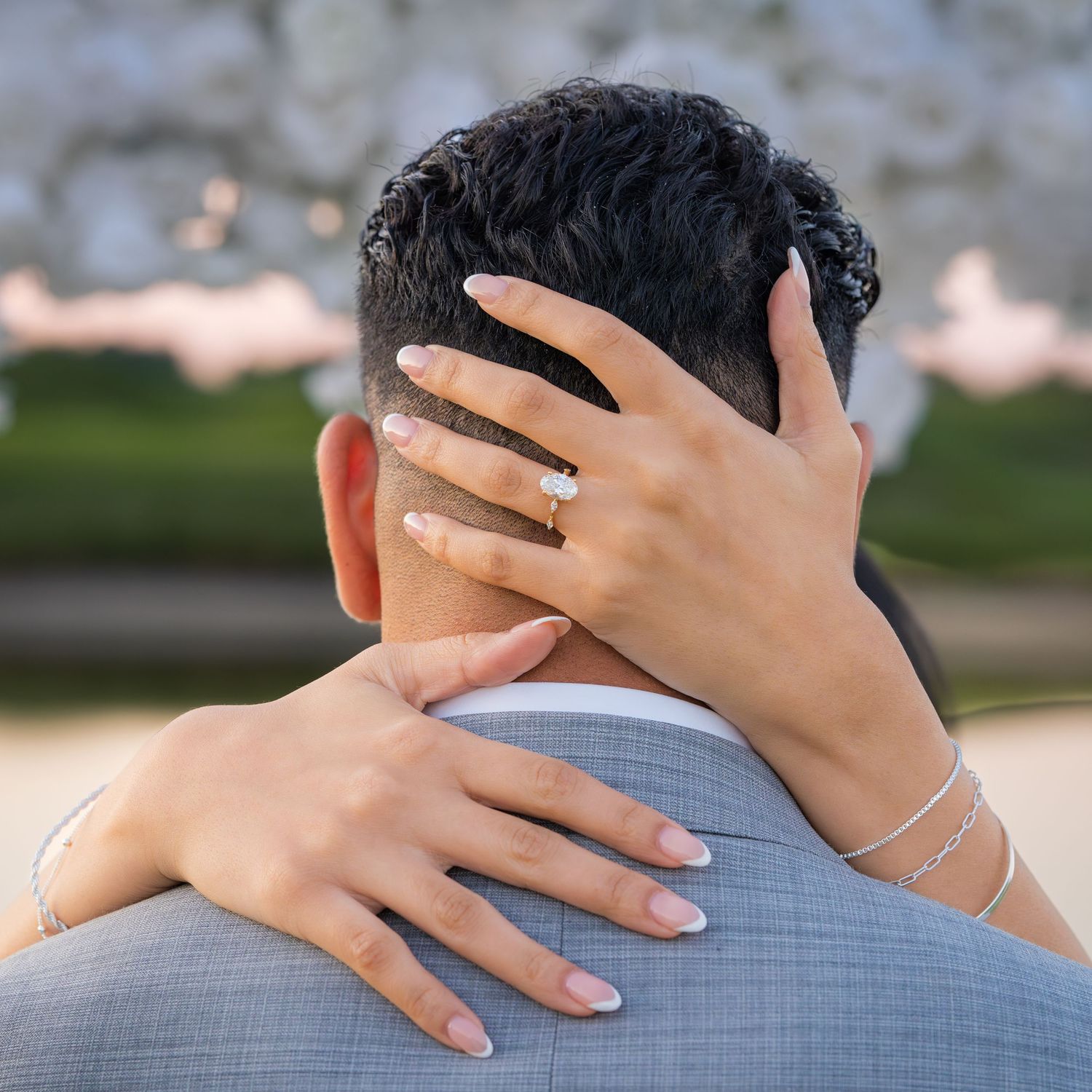 Close up of hands embracing on grey suit jacket with ring visible.