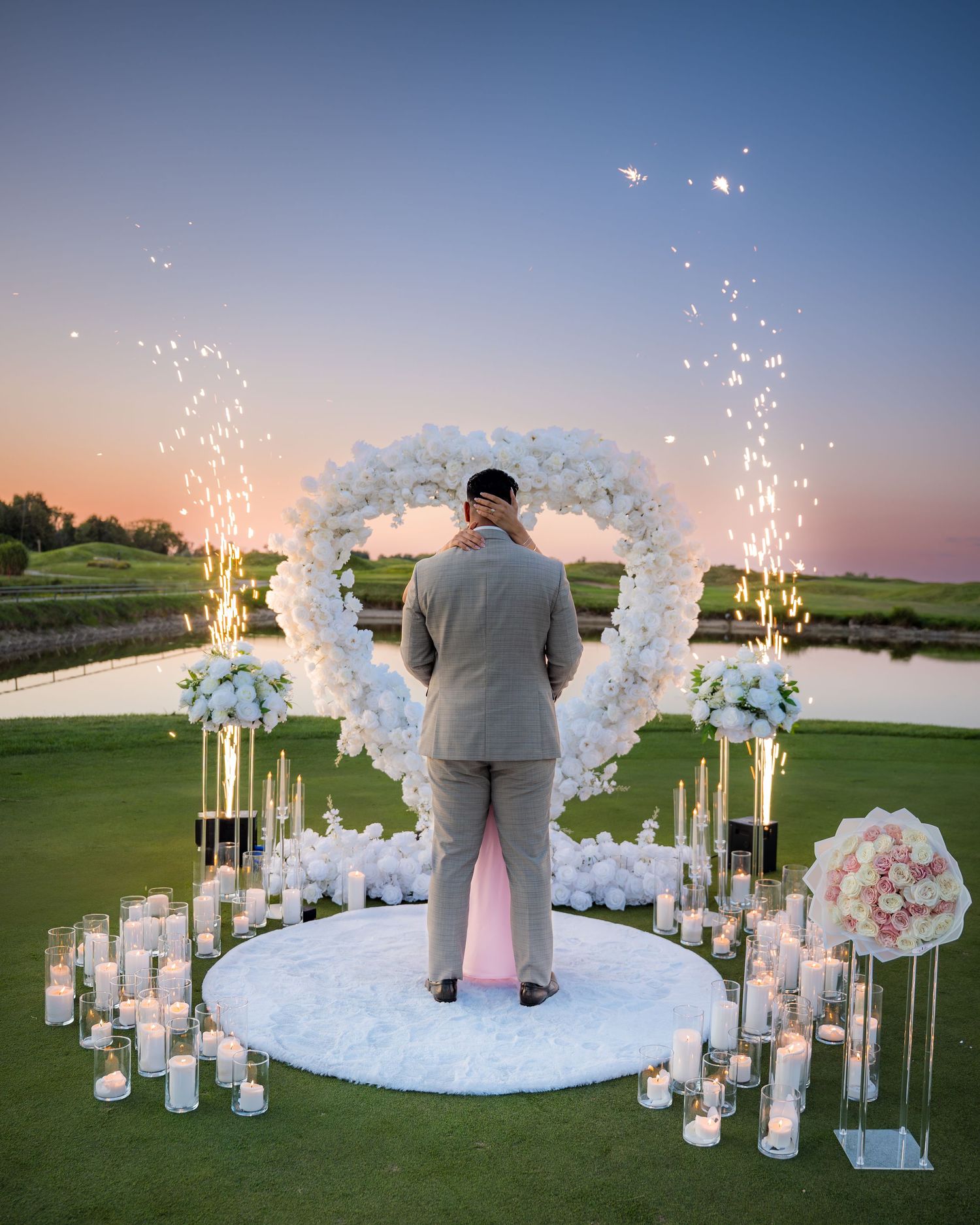 Beautiful proposal setup with white floral arch and candles against sunset golf course backdrop.