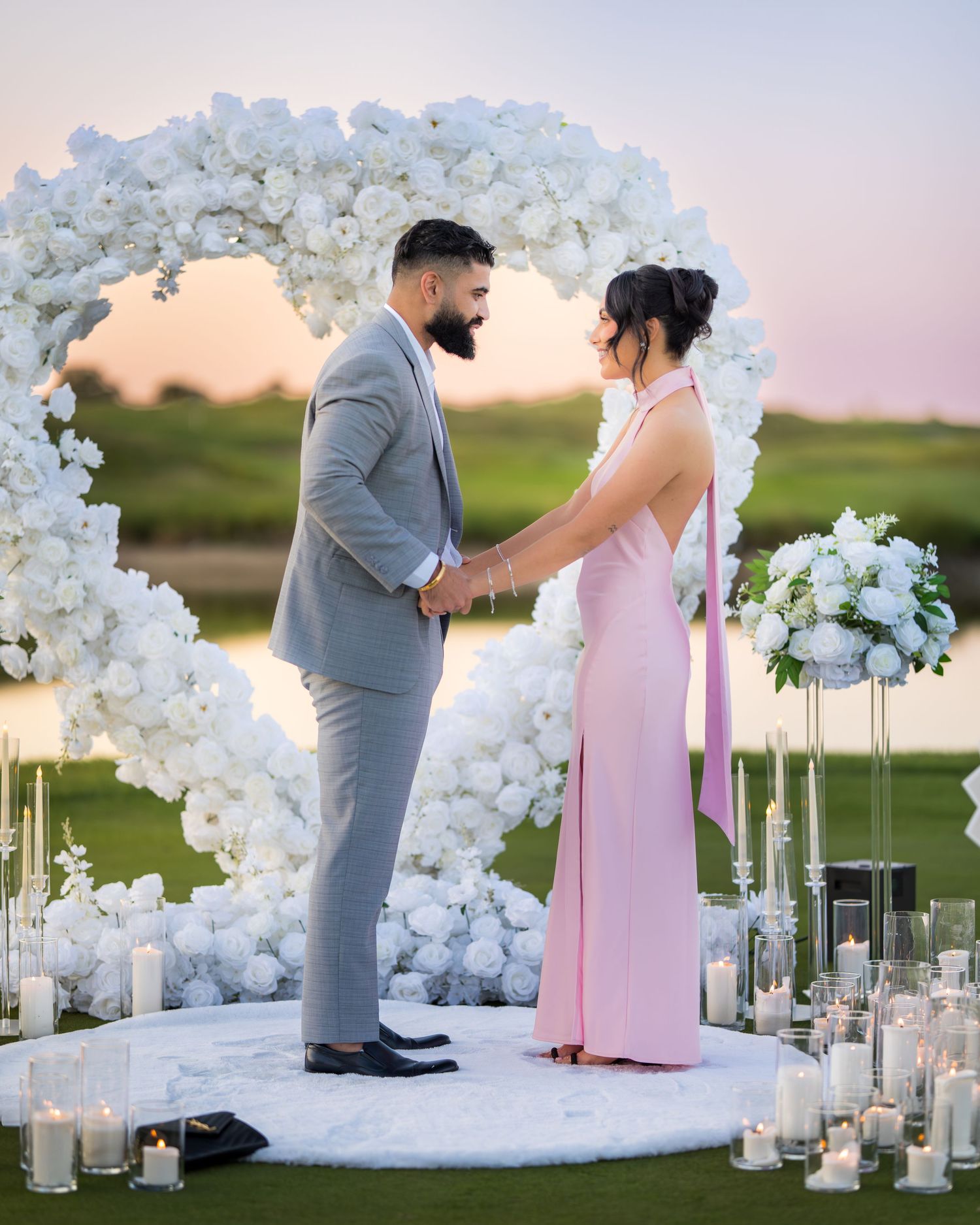 A beautiful proposal setup with white floral arches and candles at sunset.