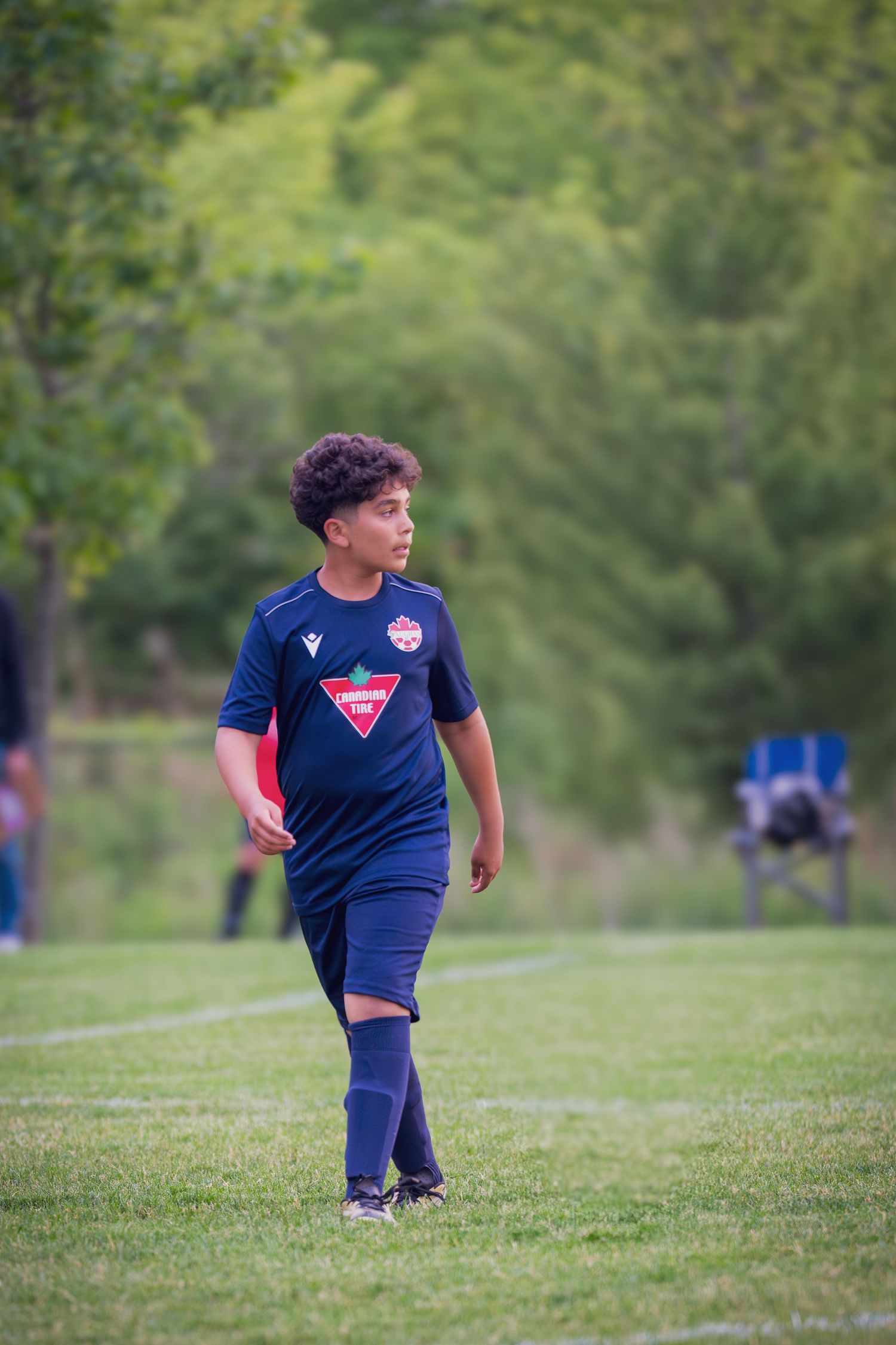 Young soccer player in navy blue uniform stands on grass field during outdoor practice session.