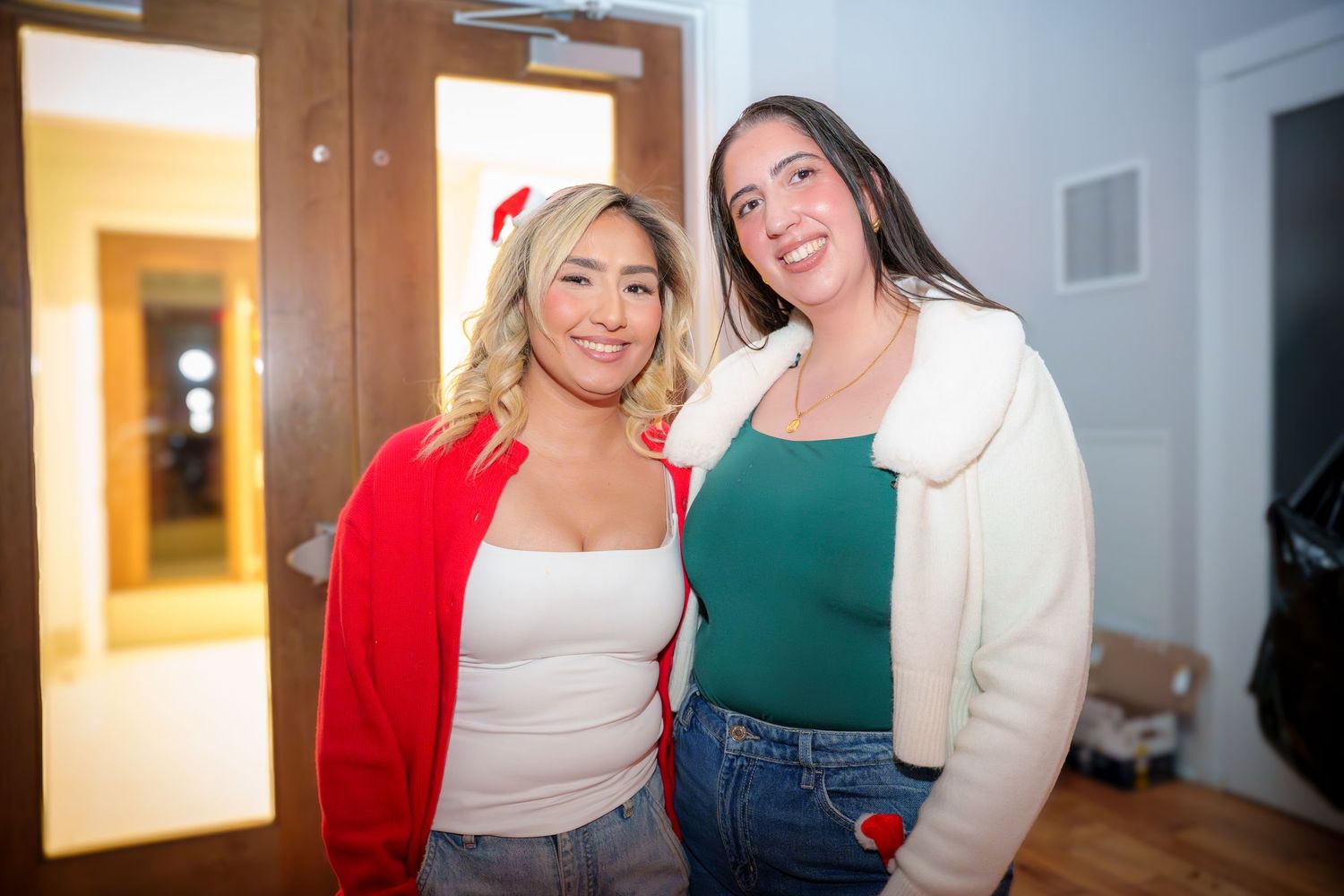 Two friends pose together at an indoor party wearing casual winter attire.