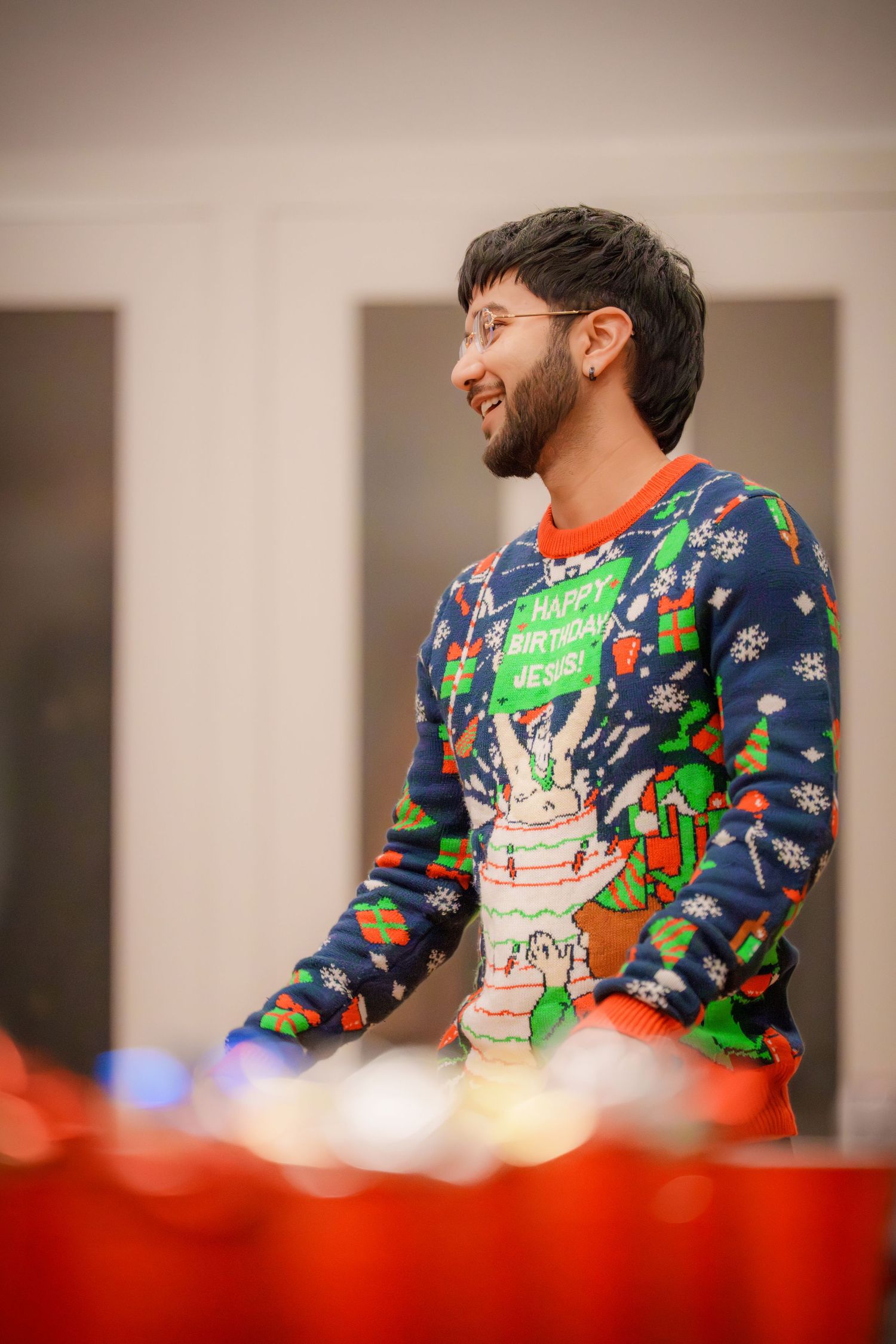 Person wearing festive blue holiday sweater with colorful decorations at a party.