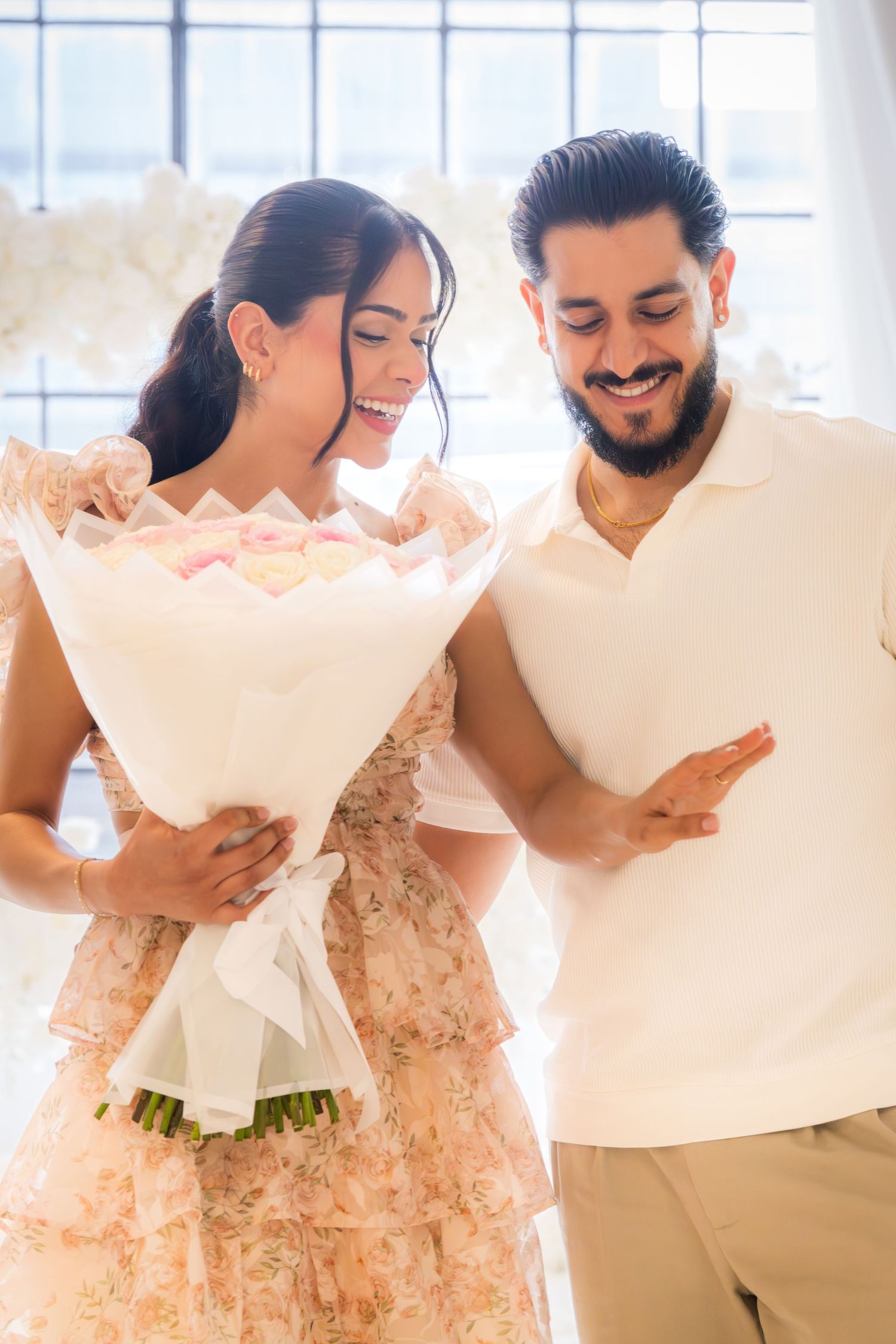 Smiling couple sharing a moment with a large white flower bouquet in a bright floral venue.