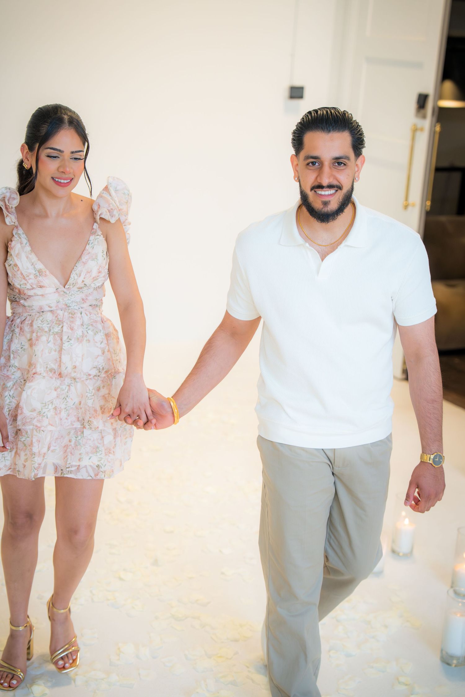 Happy couple holding hands and smiling while walking through white rose petal covered floor.