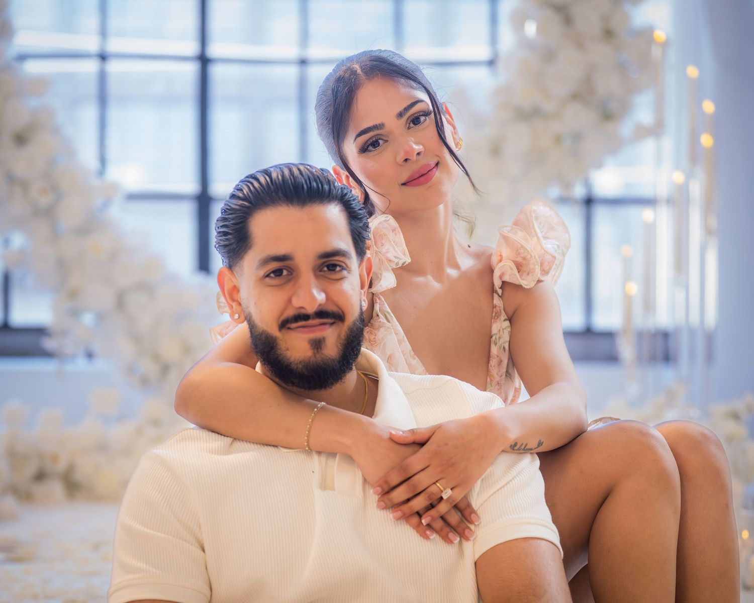 Engaged couple posing intimately surrounded by white floral decorations after proposal.