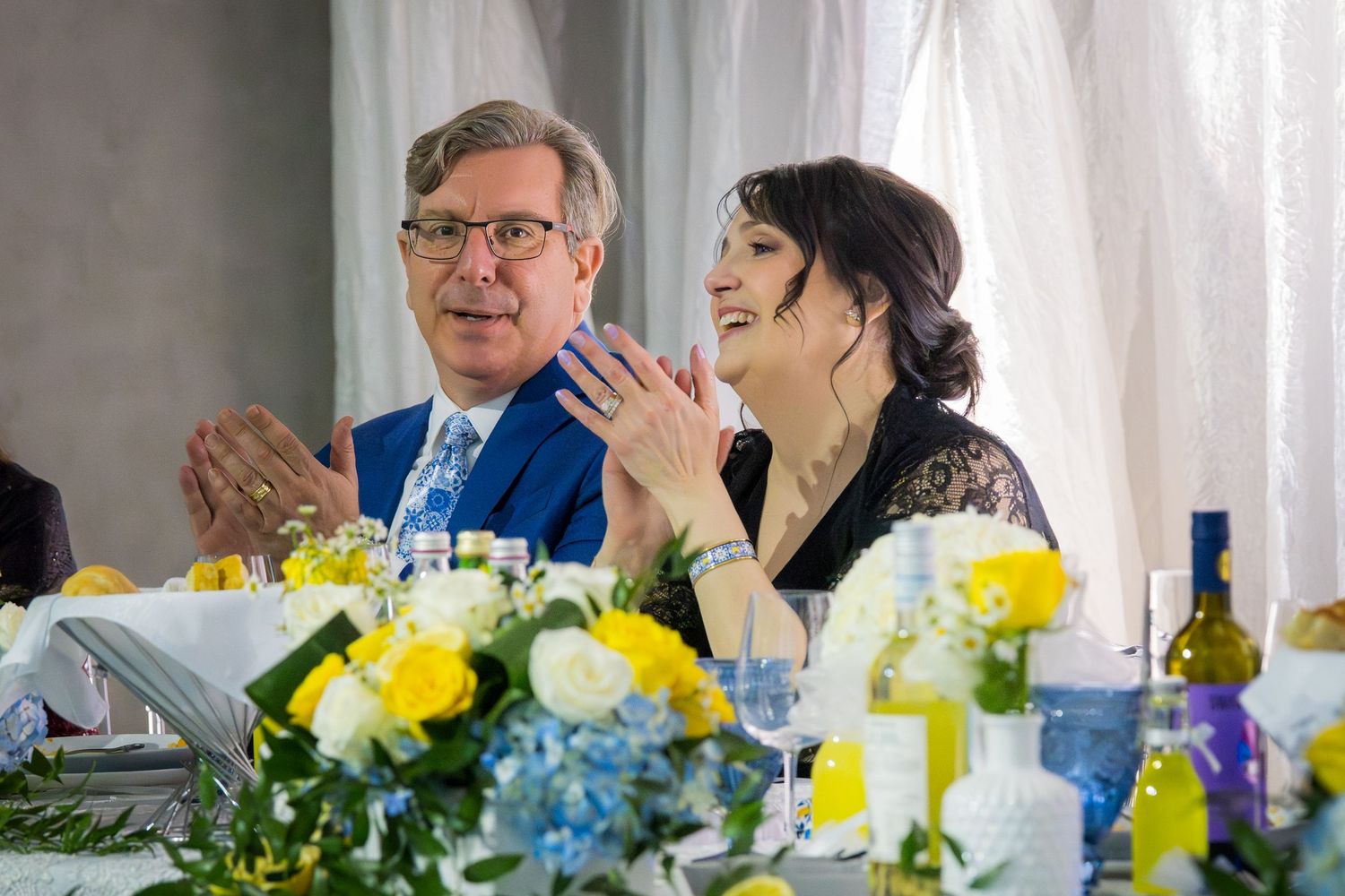 Couple smiling at a festive wedding reception table with yellow and blue floral arrangements.