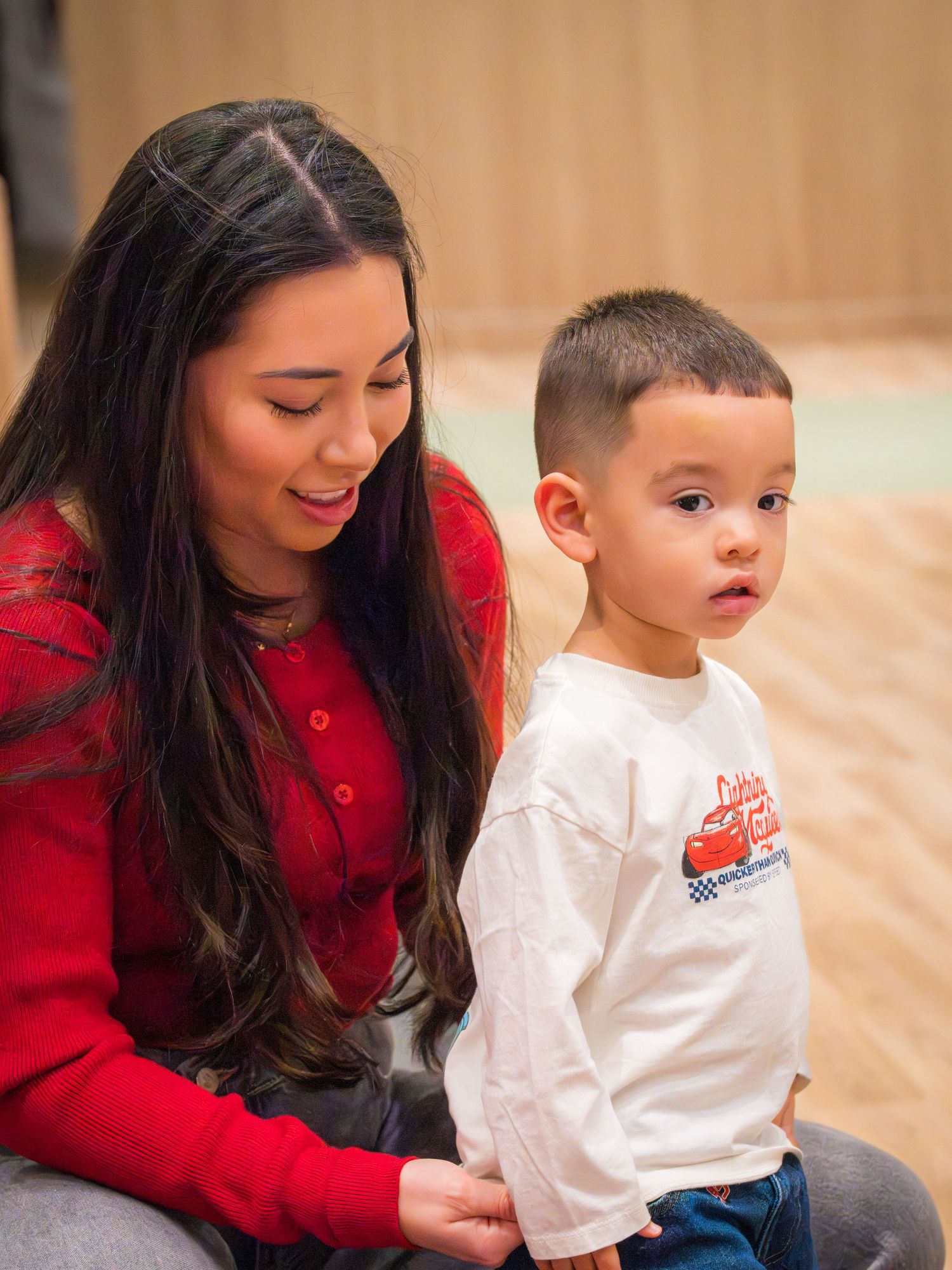 A woman in a red top smiles at a young boy wearing a Lightning McQueen shirt at a birthday party.