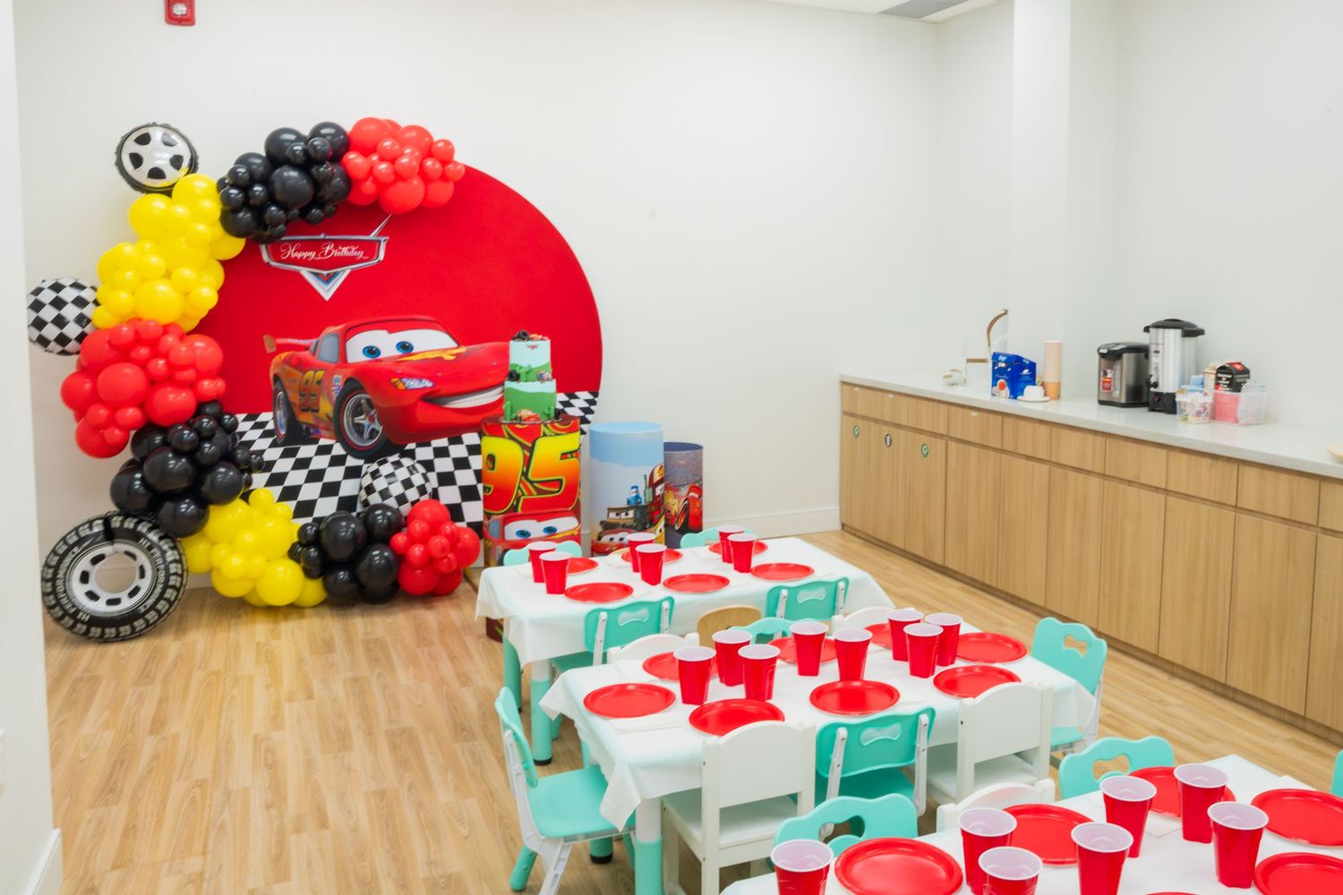 Cars-themed birthday party room with Lightning McQueen backdrop, balloon arch, and decorated tables with red cups.