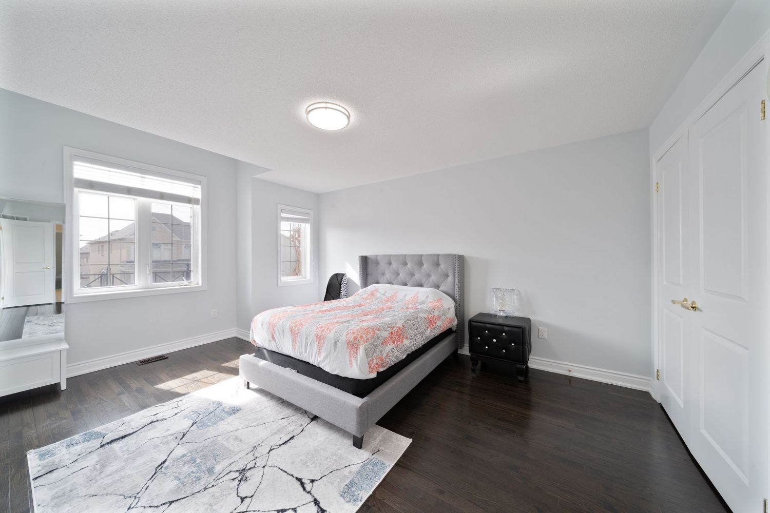 Modern white bedroom interior with grey tufted headboard, recessed lighting and minimalist decor.
