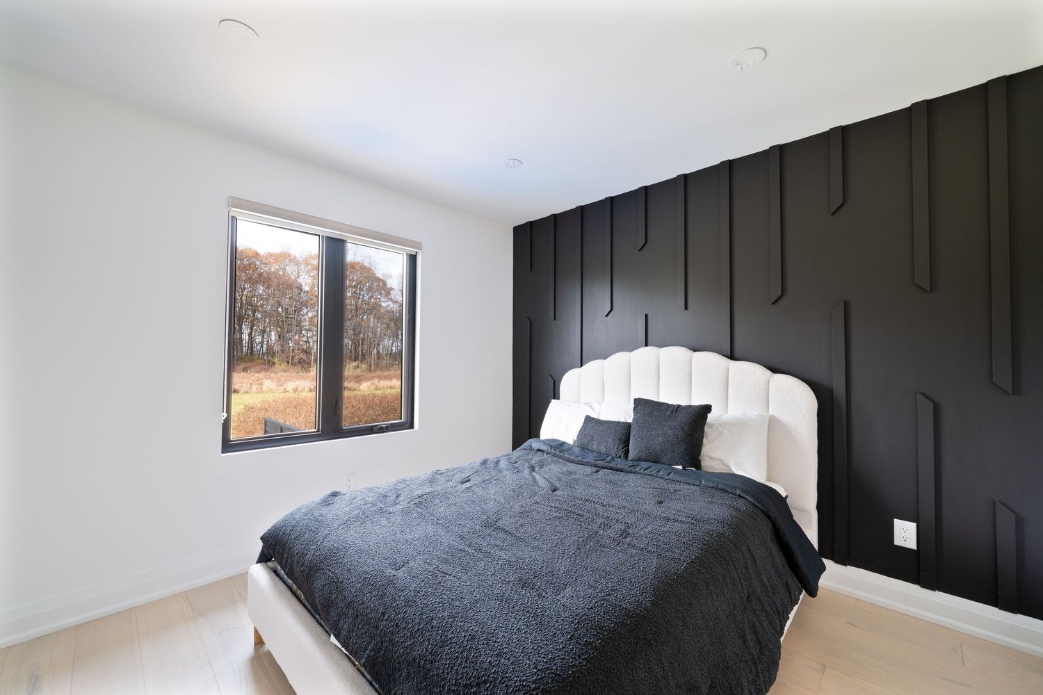 Modern bedroom interior with black accent wall, white bedding, and natural light streaming through window.