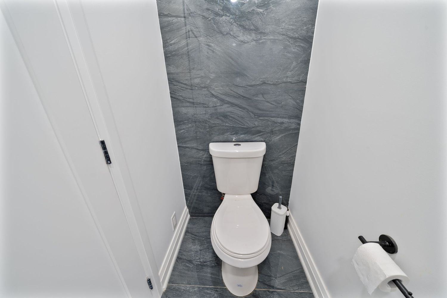 A modern white bathroom interior with toilet, vanity, and dark gray tile floor in a minimalist style.