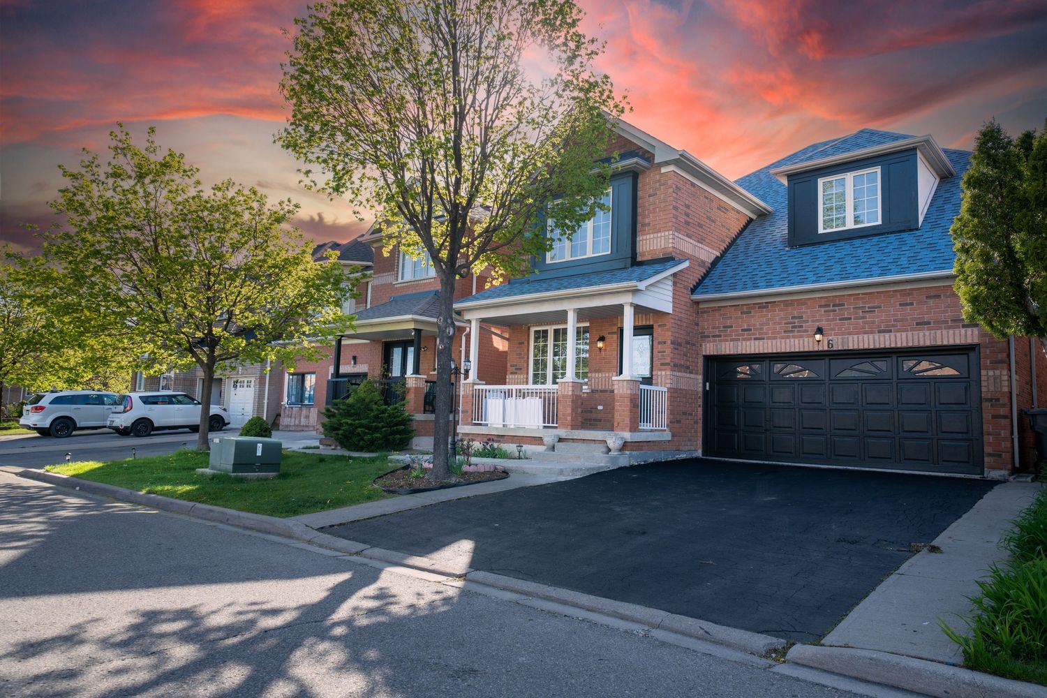 A series of residential homes with driveways and garages at sunset with dramatic orange and pink clouds in the sky.