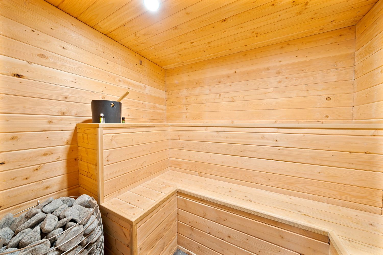 Interior of a modern wooden sauna with light pine walls, benches, and ceiling illuminated by a warm overhead light.