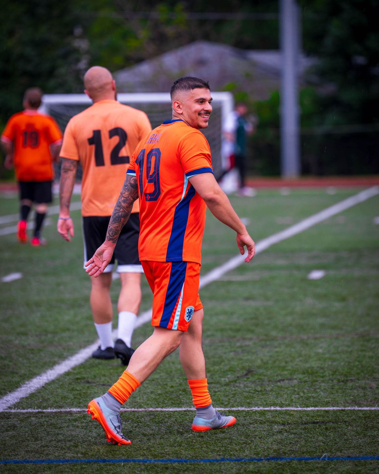 Athletes in orange jerseys running drills during soccer practice.