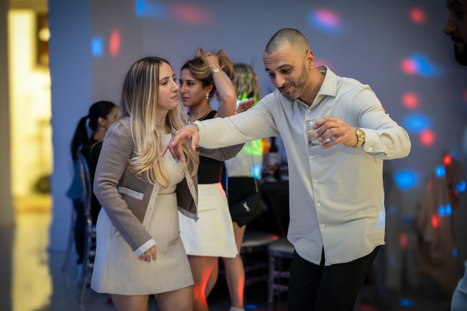 People dancing and celebrating at a party with colorful lighting effects in the background.