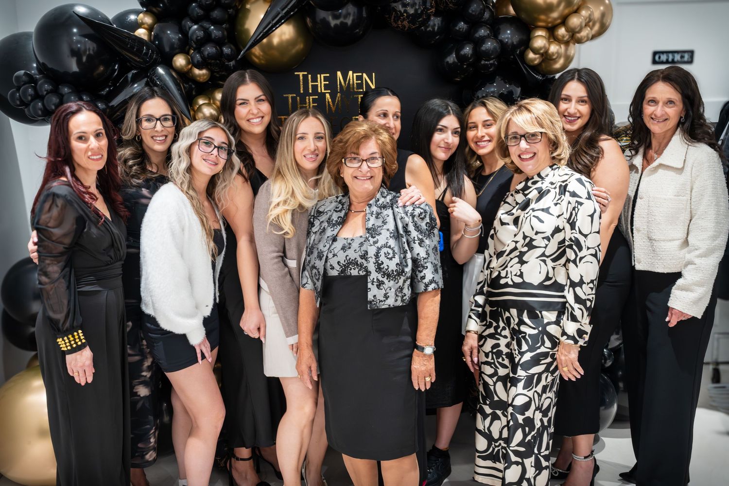 Large group celebration photo with black and gold themed party decorations.