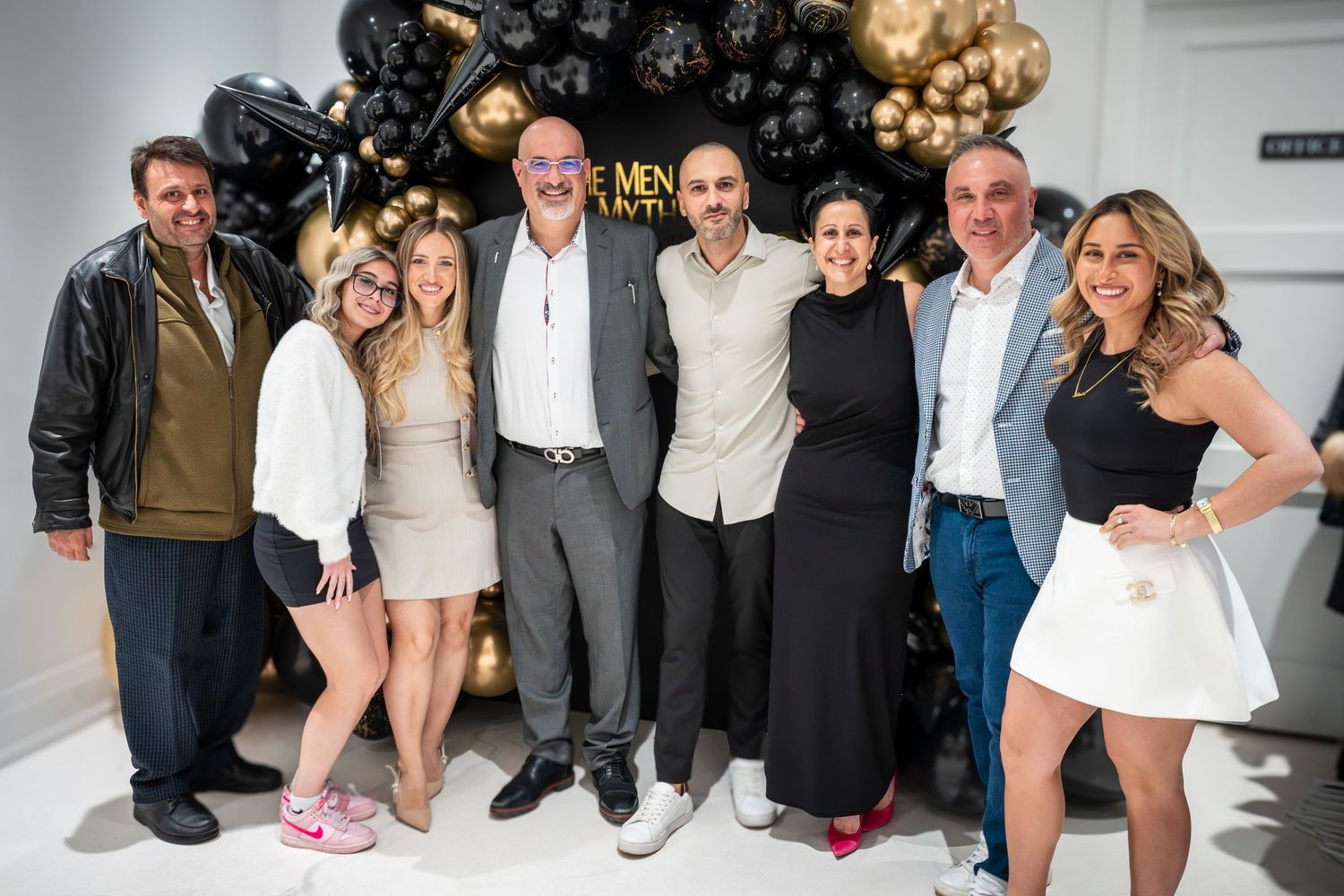 Event guests posing together at celebration with elegant black and gold balloon decor.
