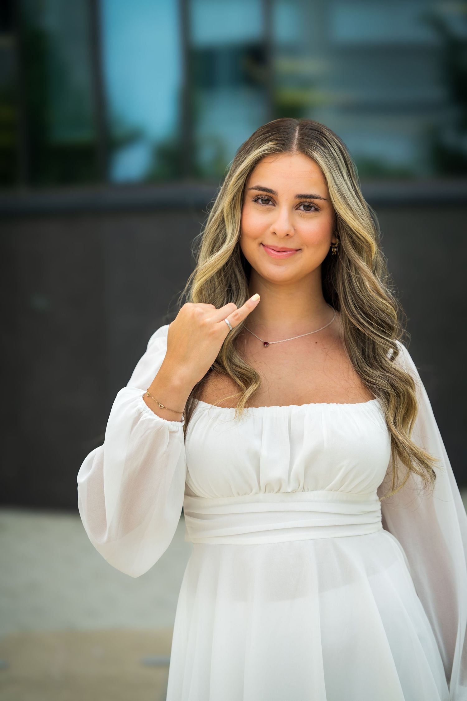 Portrait of graduate in romantic white dress with long wavy hair styled elegantly.