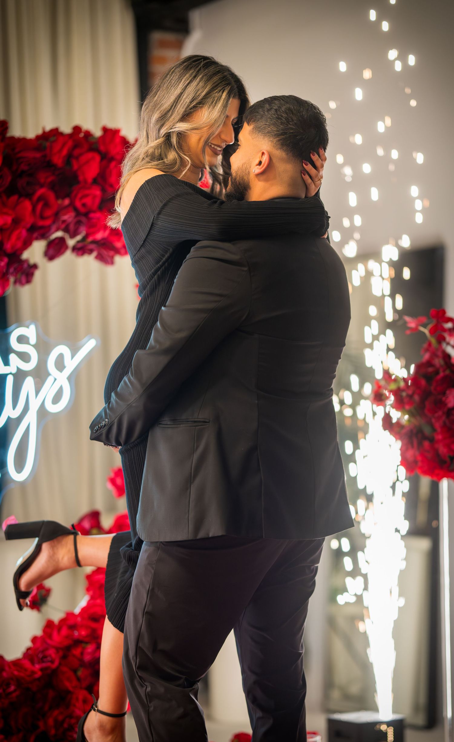 Proposal scene with sparklers, neon lighting, and dramatic red rose wall decoration.