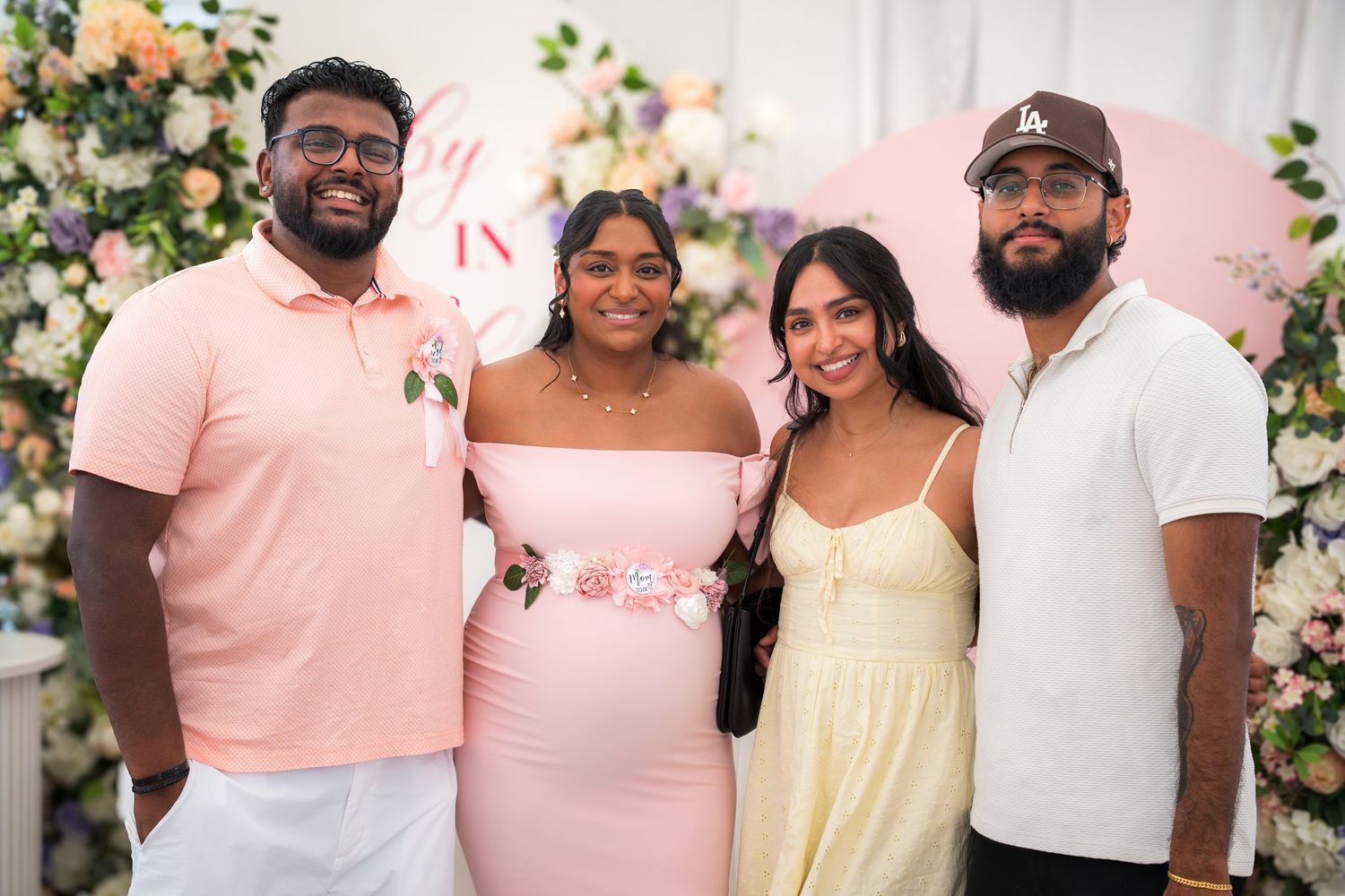 A group celebrating at a baby shower with pink decor and floral arrangements.