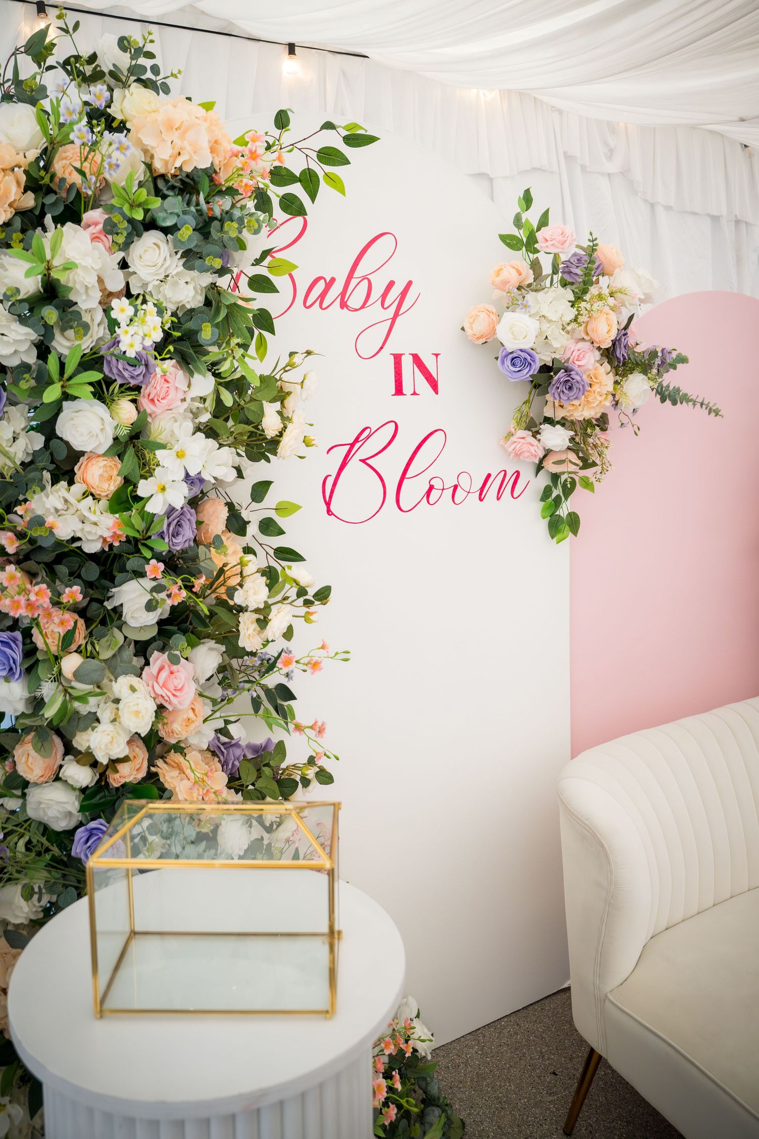 Elegant white sofa with floral arrangements and 'Baby Bloom' text on pink backdrop.