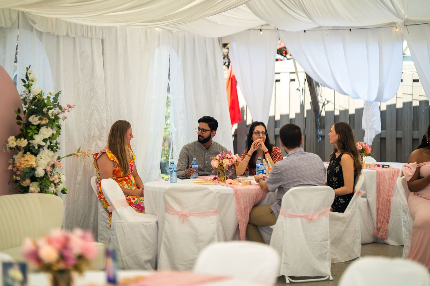 Indoor baby shower celebration with guests mingling under white tent decorations.