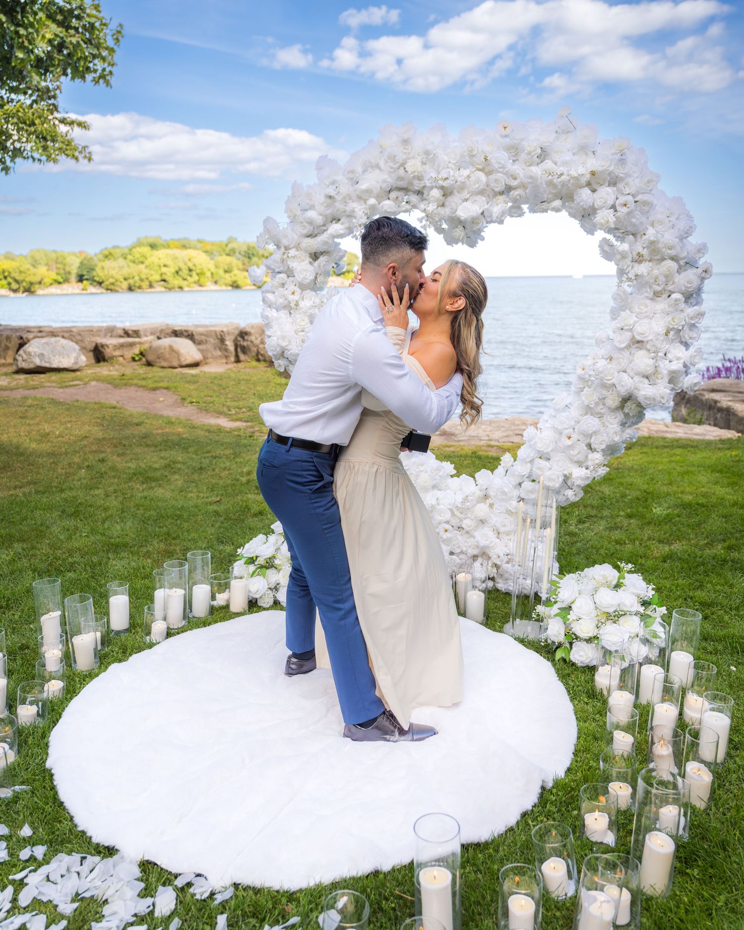 A romantic proposal setup with a white floral arch and candles overlooking the ocean.