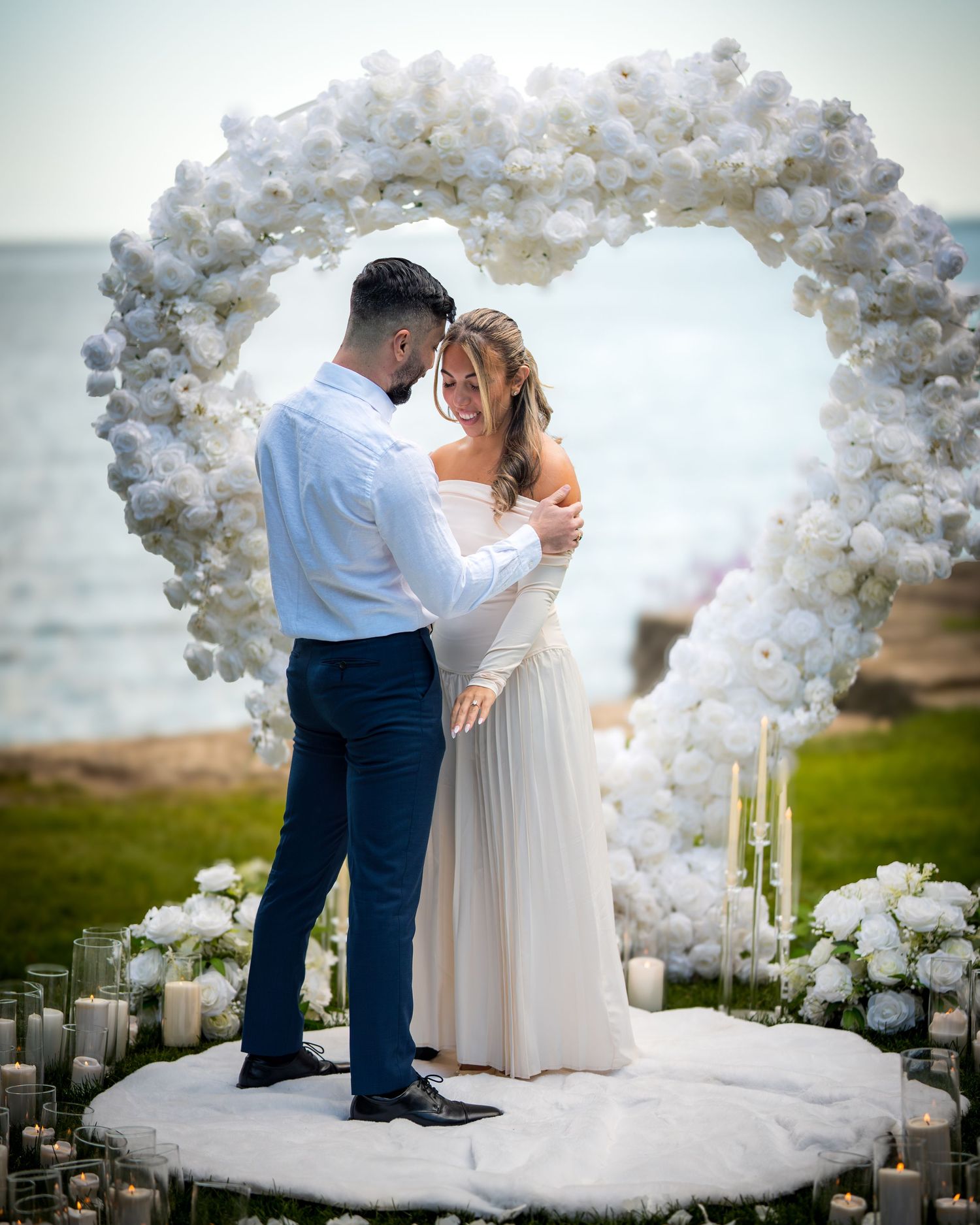 Elegant proposal setup featuring white balloon heart arch and candlelit platform overlooking the sea.